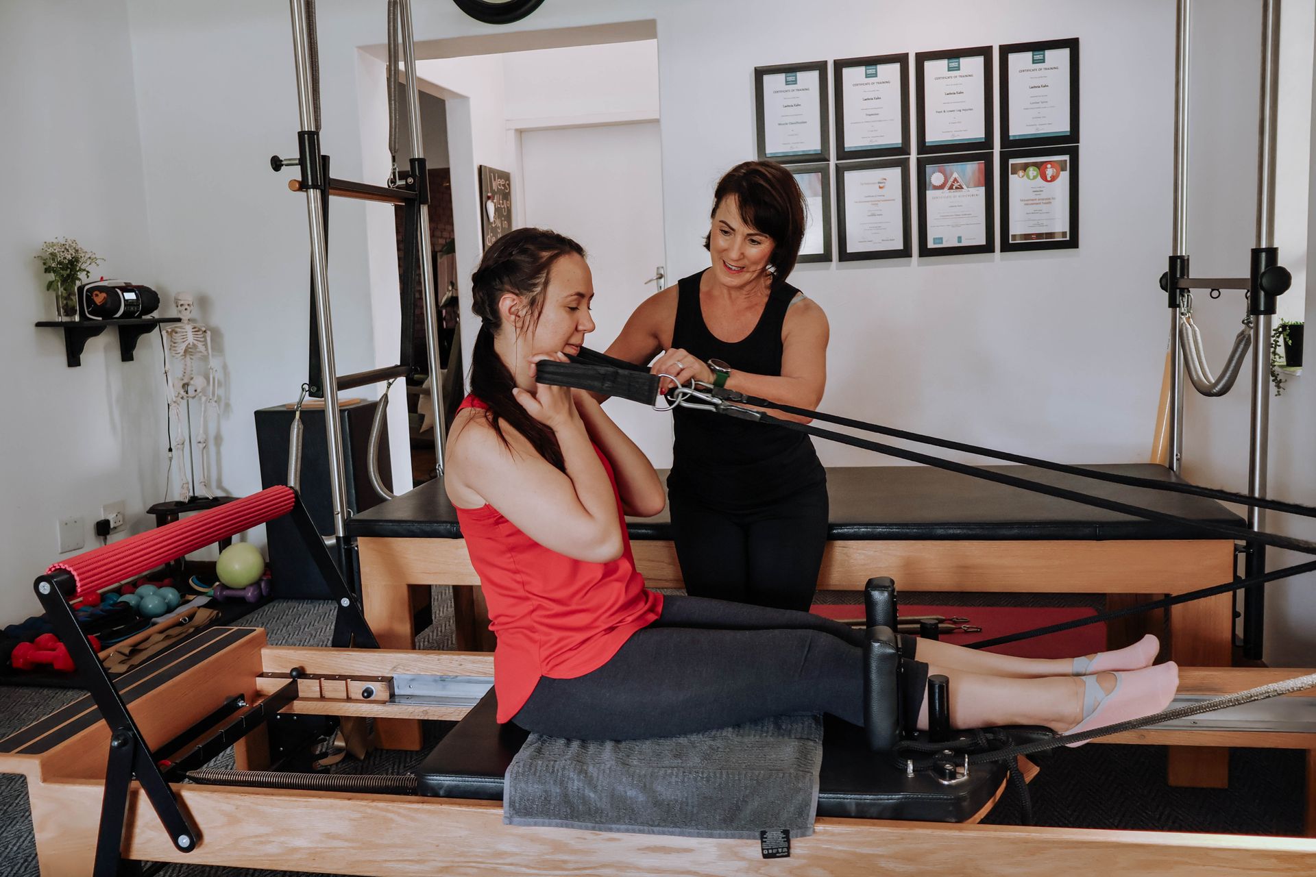Woman exercising on a Pilates reformer while instructor guides her in a studio
