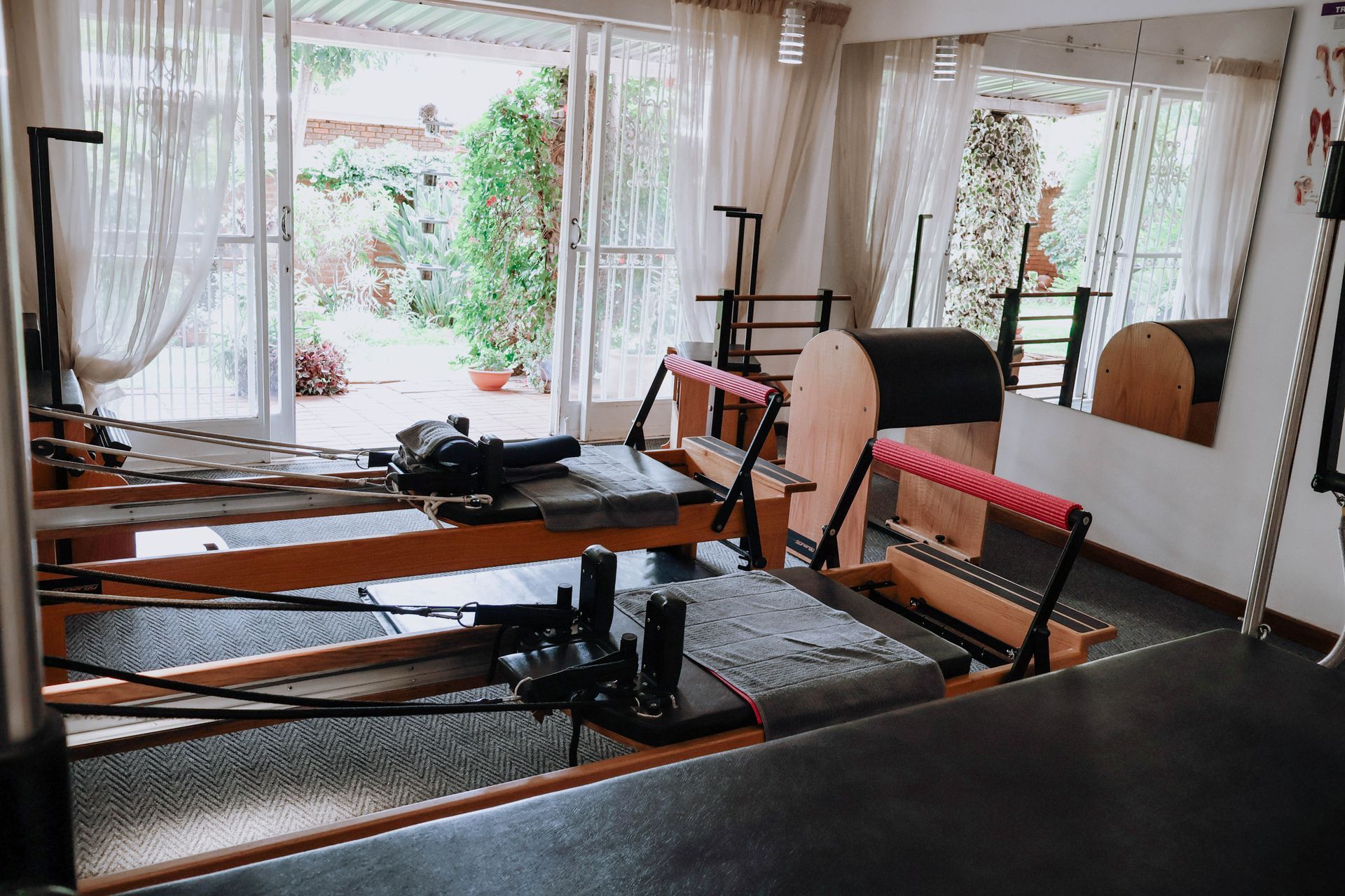 Pilates reformer equipment in a bright studio with mirrors, windows, and sheer curtains