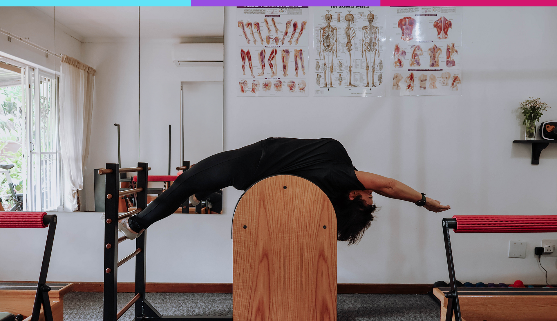 Person in black shirt arching backward over a wooden bench in a bright exercise studio.