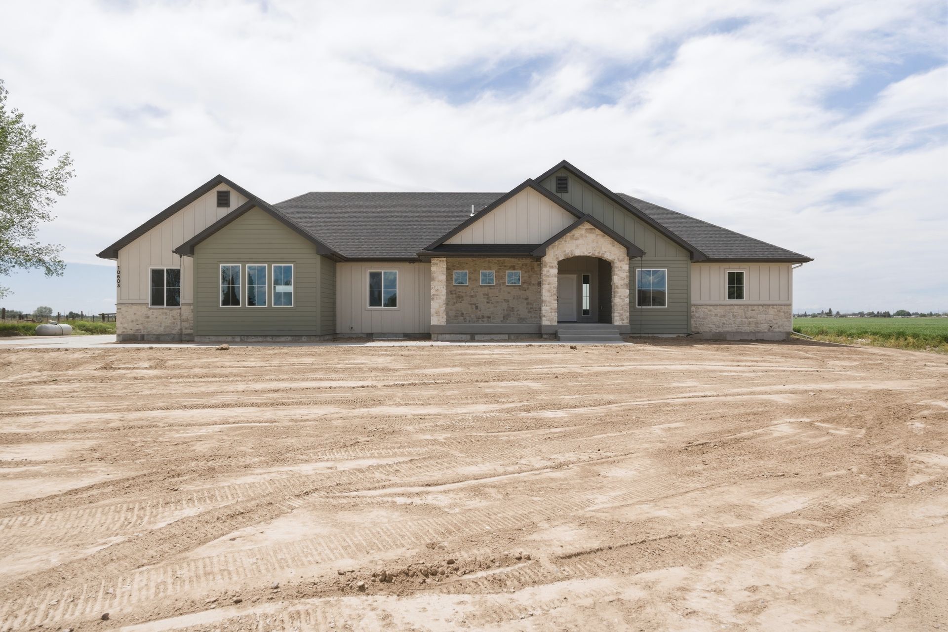 New single-story house with stone facade on a bare dirt lot under a cloudy sky
