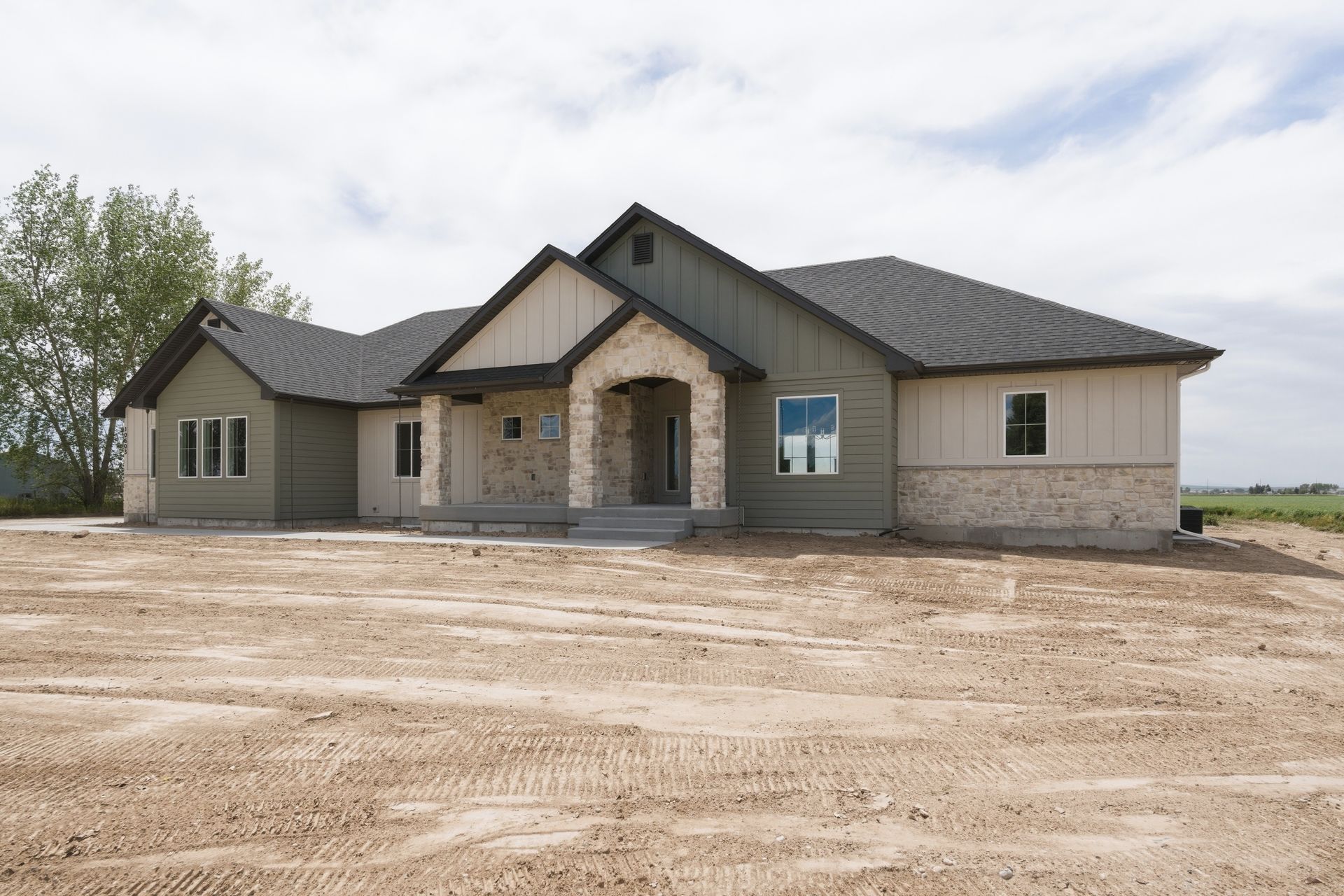 Newly built gray house with stone entry and unfinished dirt yard