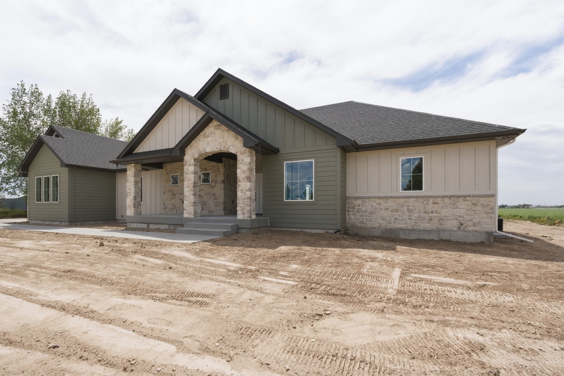 Modern single-story house with stone entry, gray siding, and dirt lot under construction