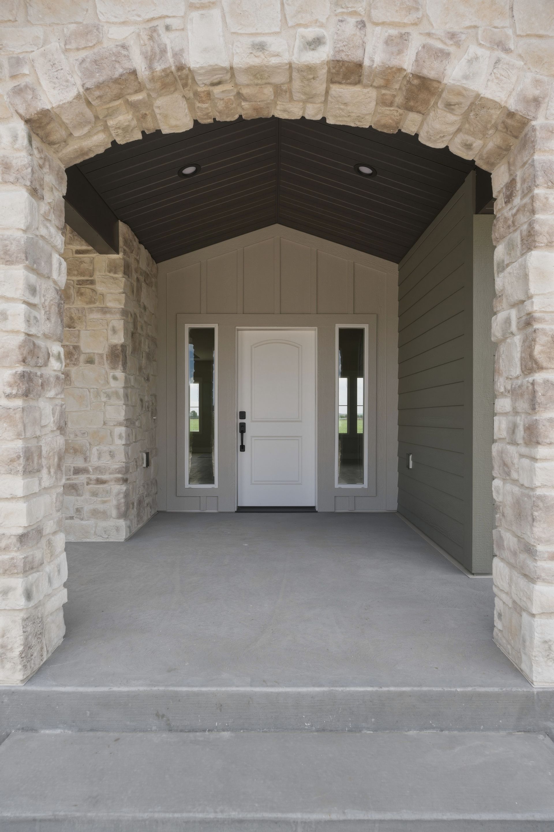 Stone arched entryway with covered porch, white front door, and side windows.