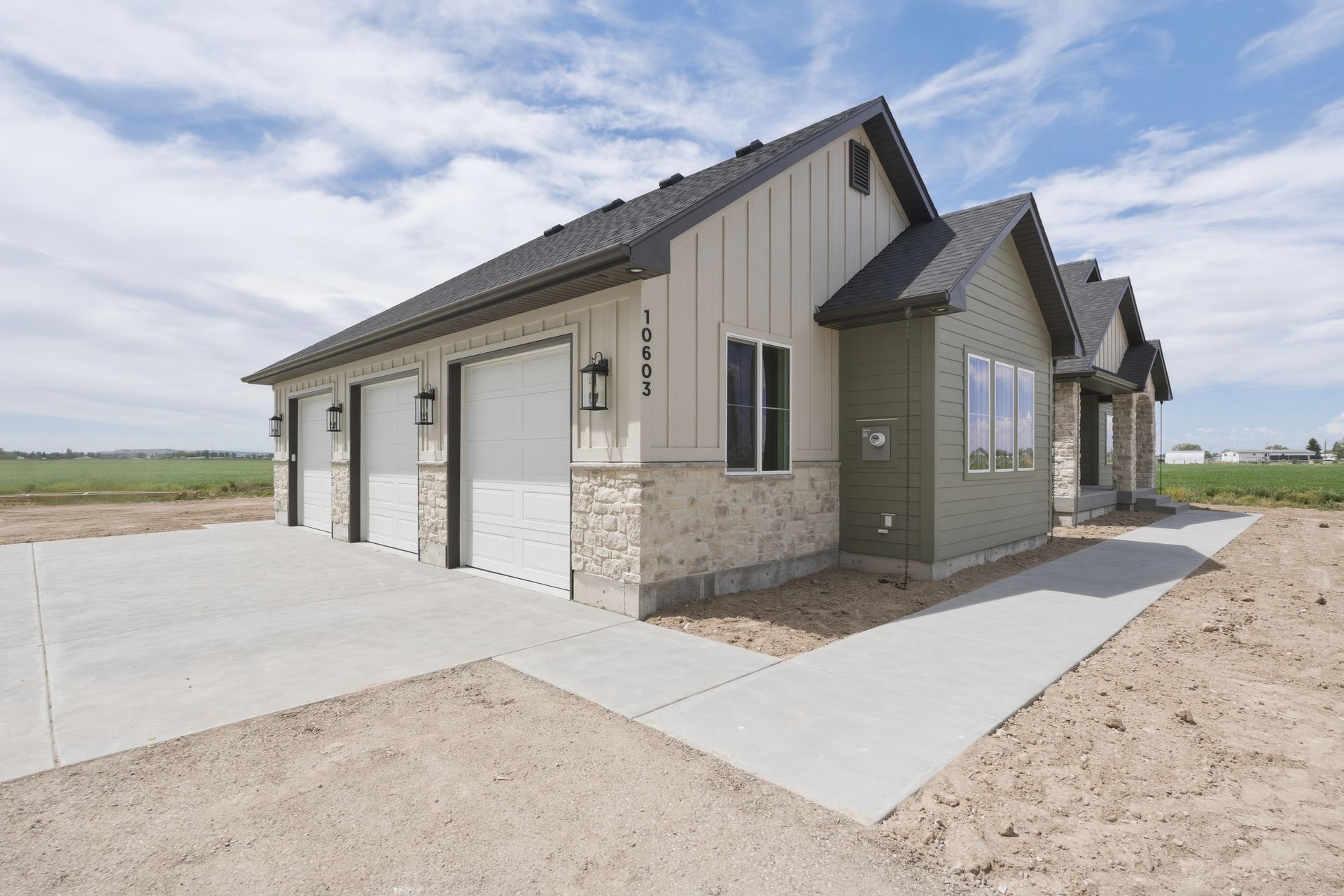 New single-story house with a gray exterior, three-car garage, and concrete driveway in a rural setting