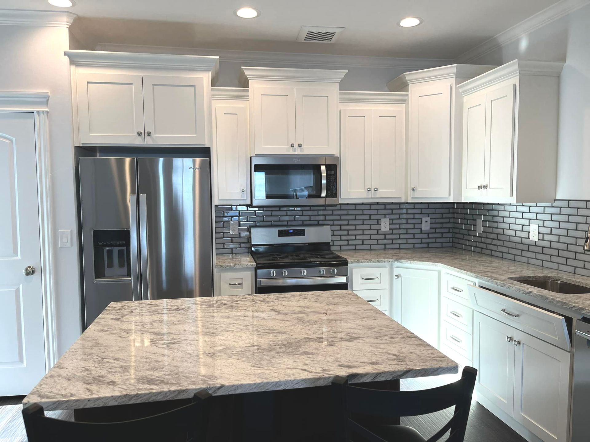 White kitchen with stainless steel appliances, granite countertops, and a central island.