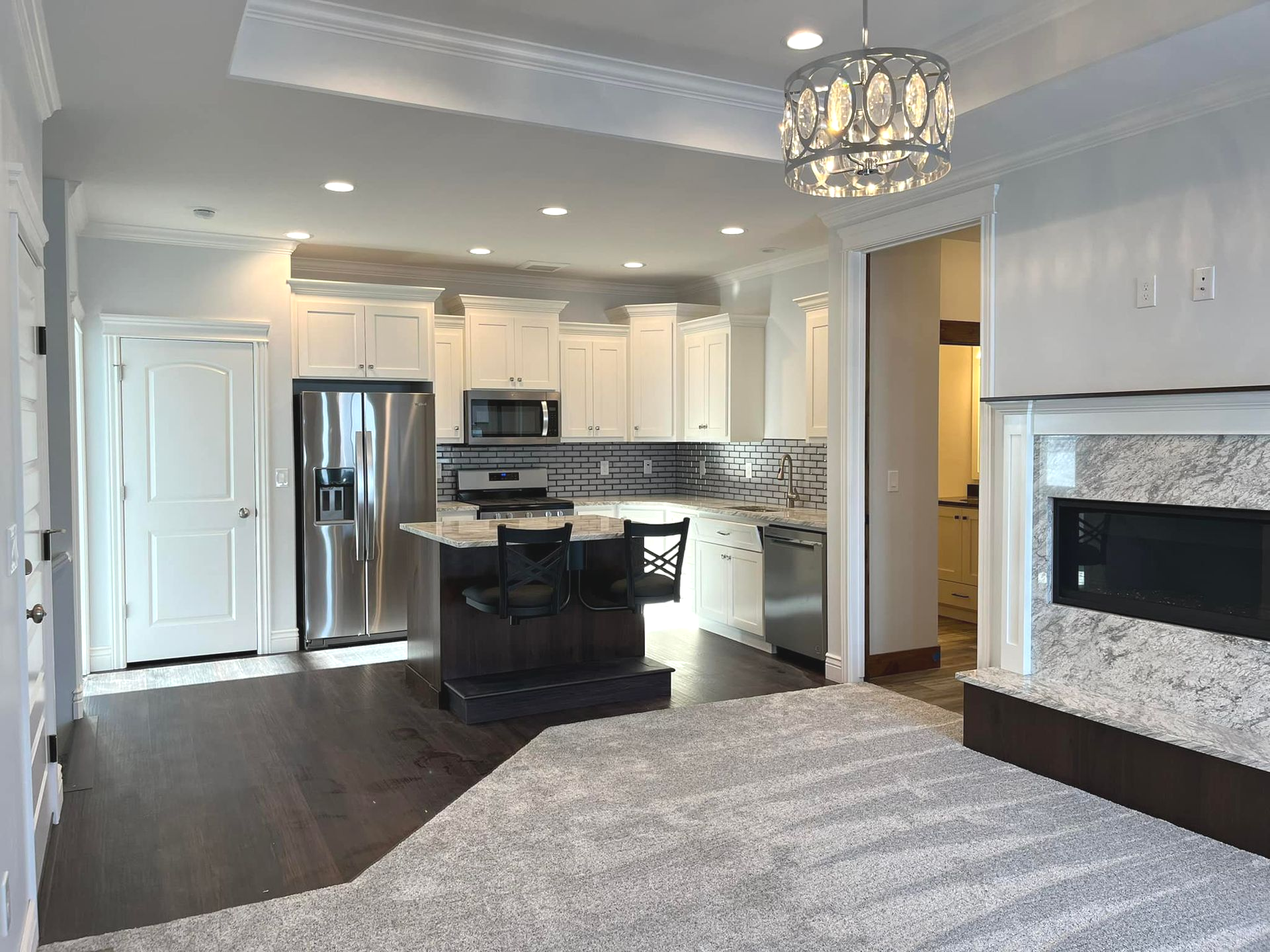 Open-concept kitchen and living area with white cabinetry, stainless steel appliances, and a gray carpet.