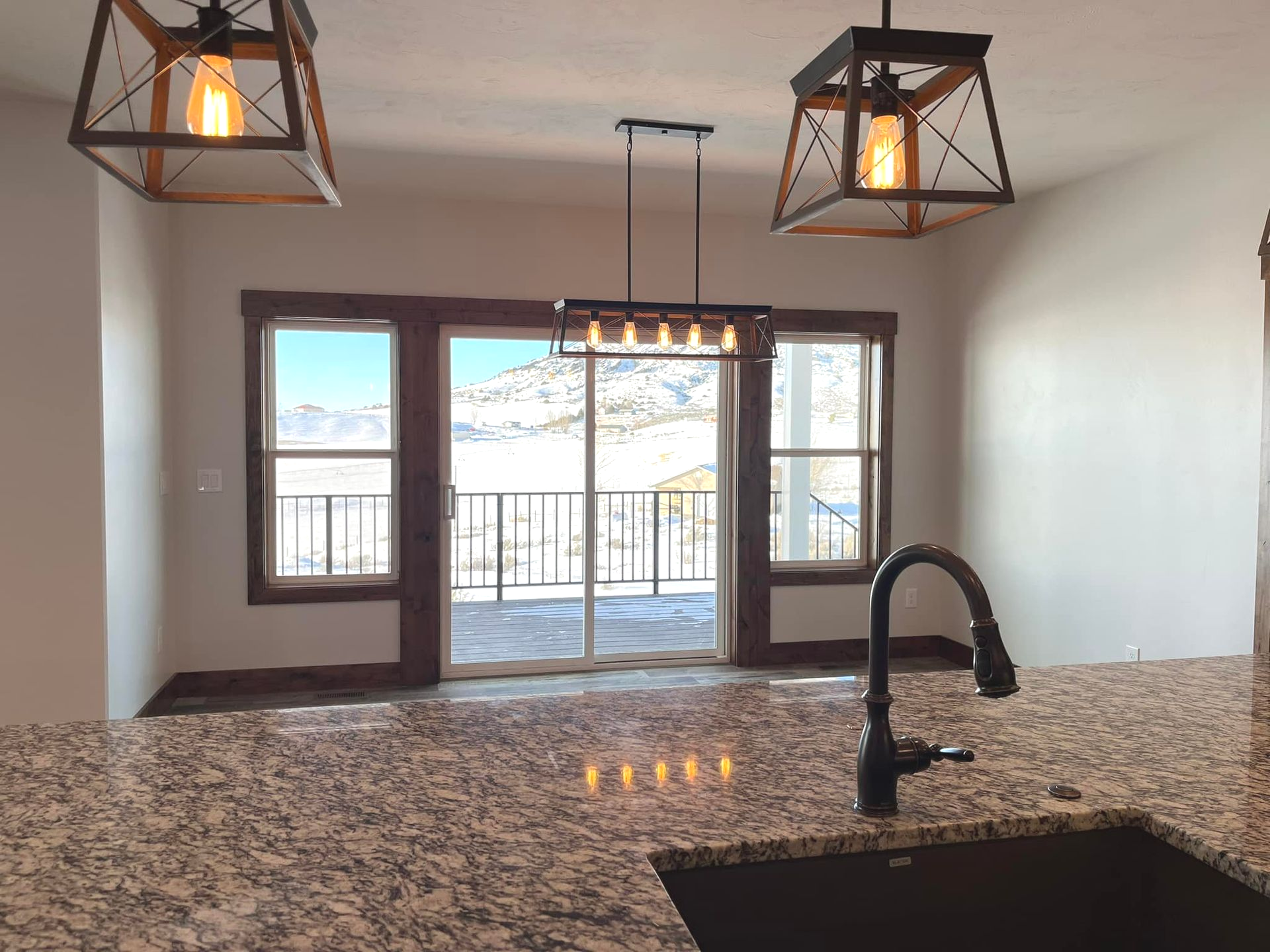 Kitchen with granite countertop, black faucet, sliding glass door overlooking snowy mountains.