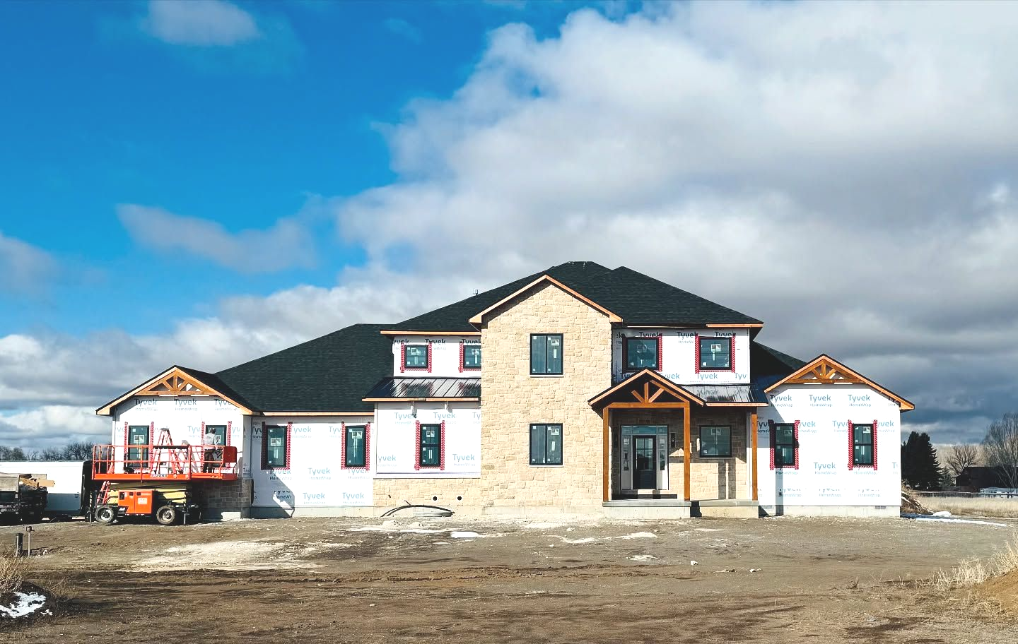 House under construction, two stories, brick and siding, blue sky.