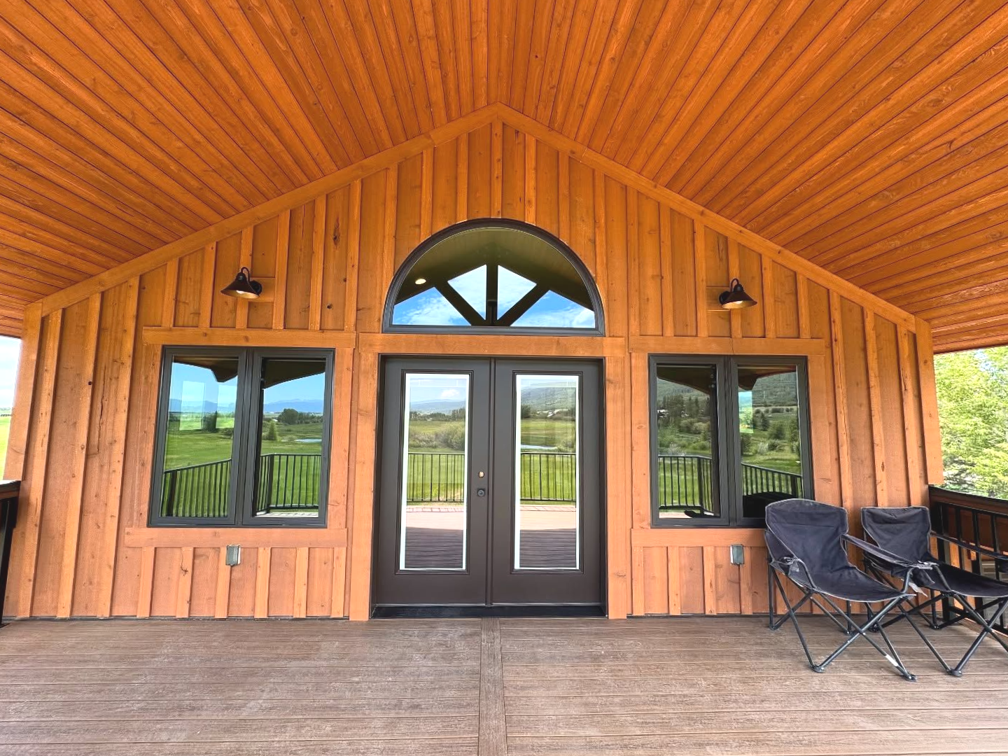 Brown wooden building exterior with arched window and double doors, flanked by windows. Two camping chairs sit in front.