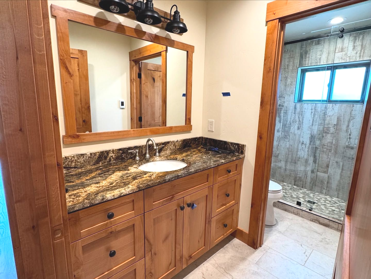Bathroom with wood vanity, granite countertop, mirror, and a view into a shower.