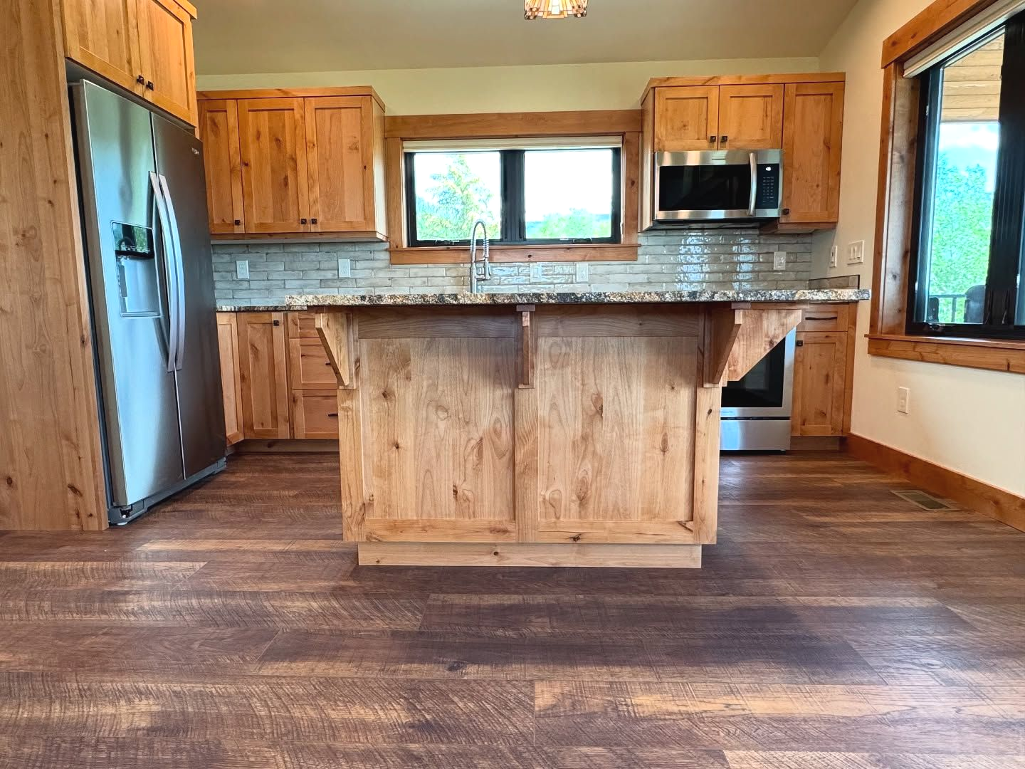 Kitchen with wood cabinets, stainless steel appliances, island, and wood floors.