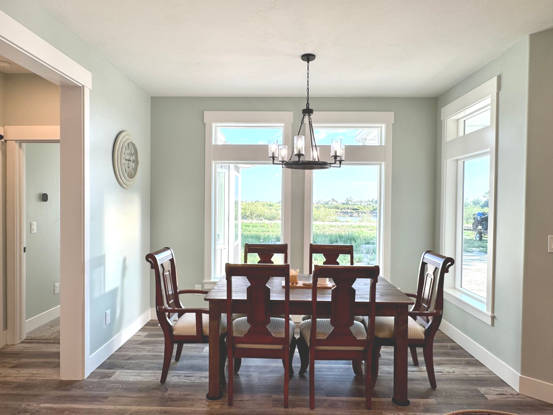 Dining room with wooden table, six chairs, large windows, and a chandelier.