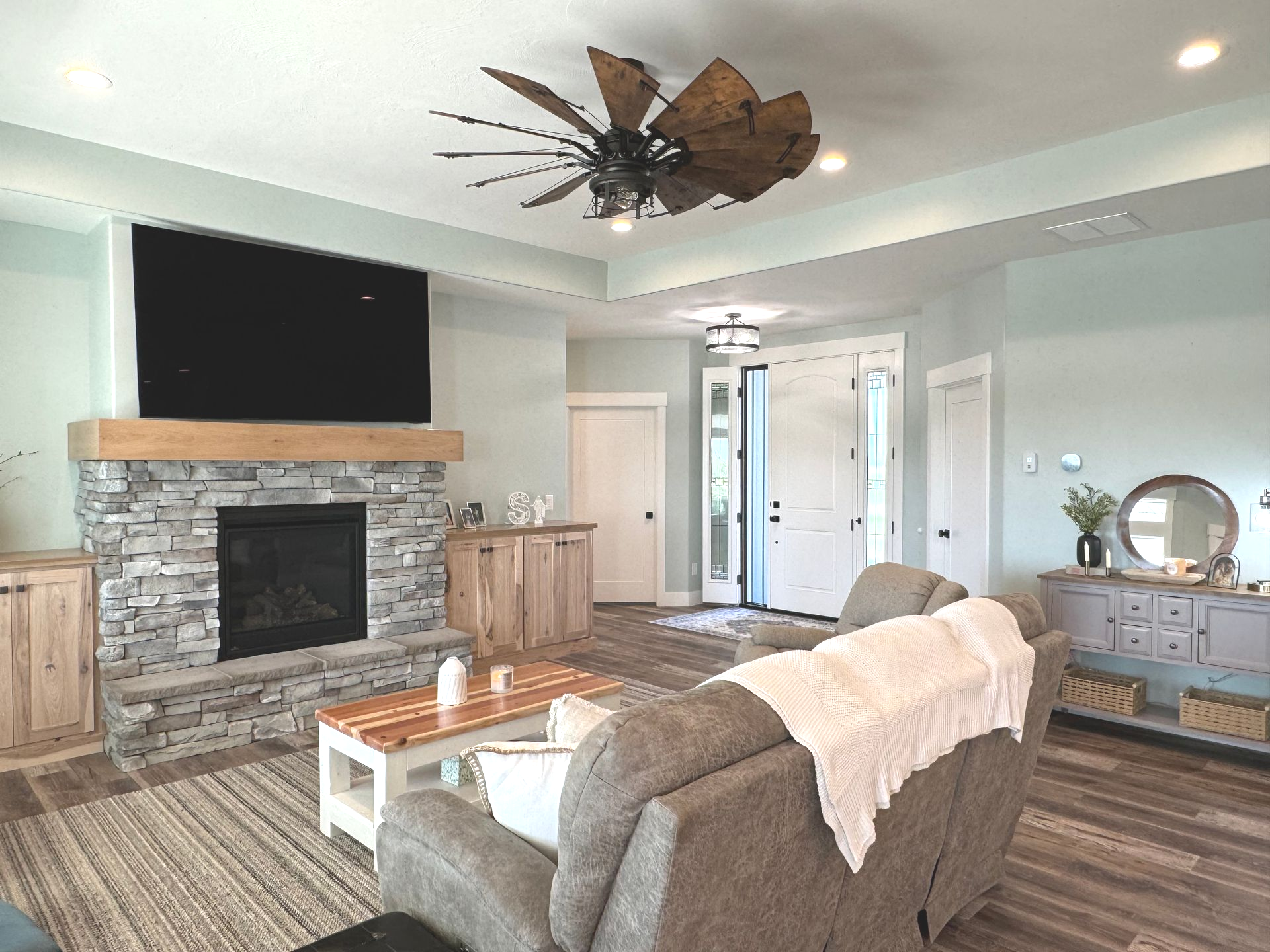 Living room with fireplace, TV, ceiling fan, and couch. Light blue walls, wood and stone accents.