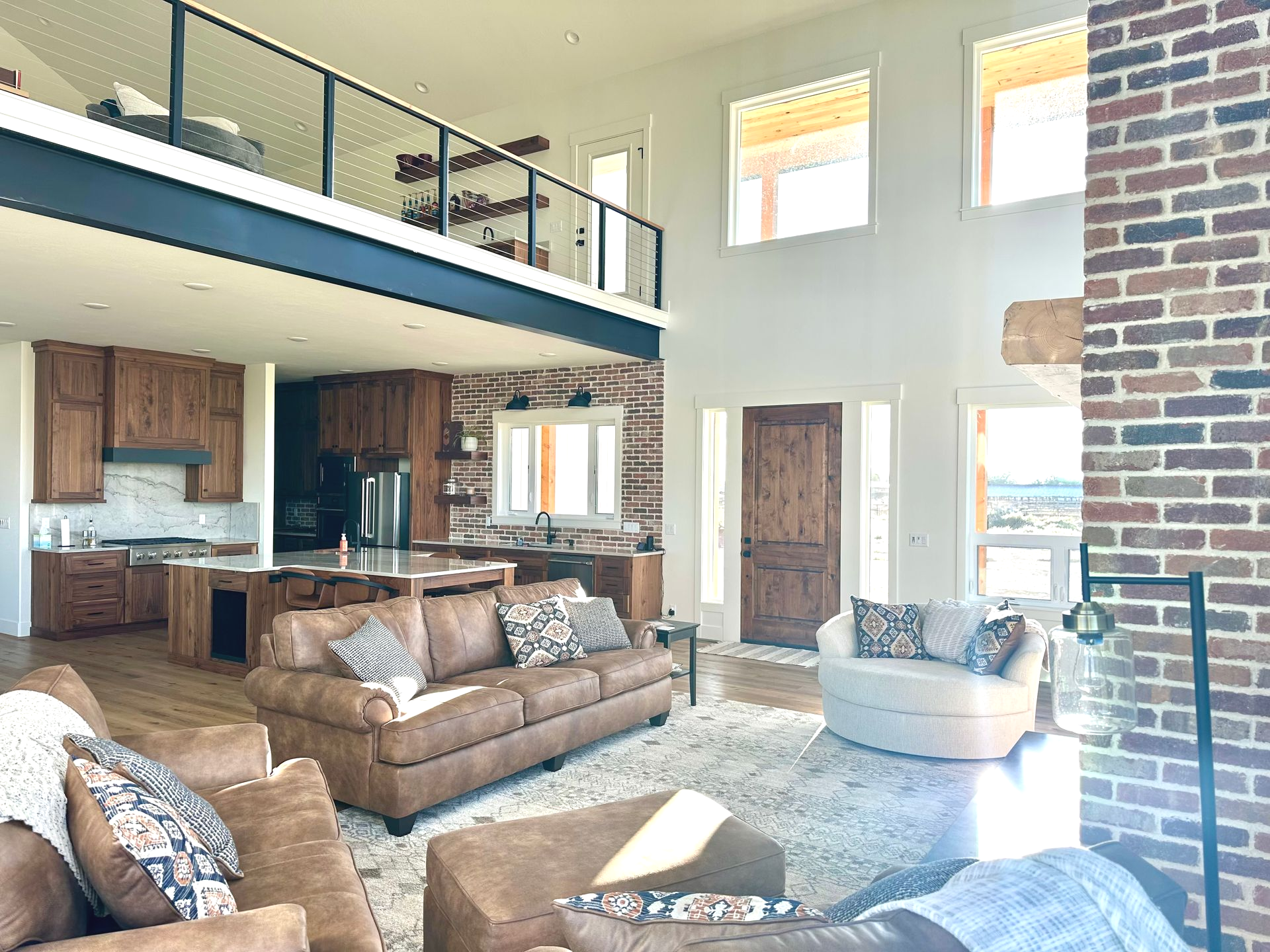 Spacious living room with leather sofas, brick accent wall, and a loft.