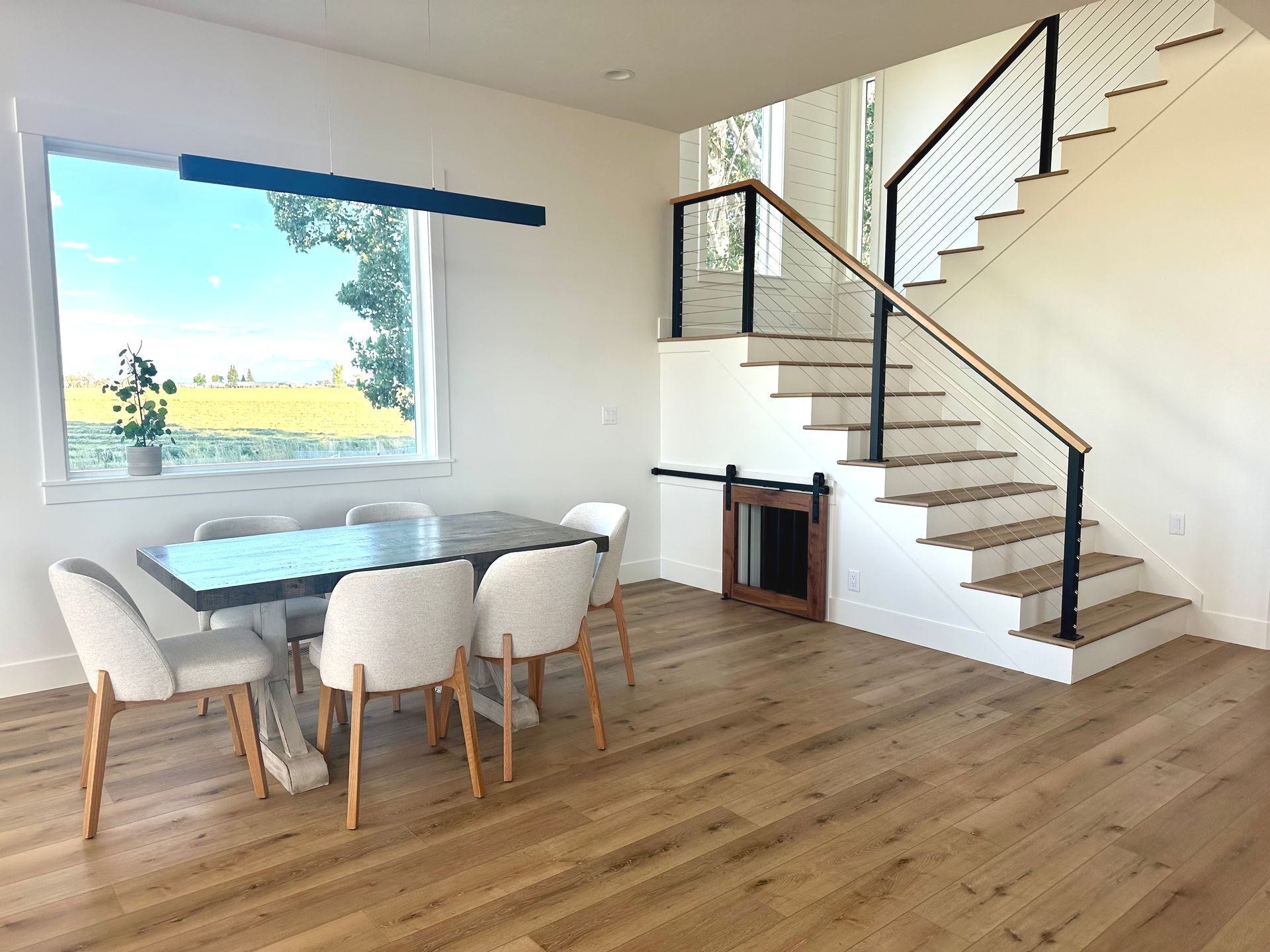 Dining area with table, chairs, window, and staircase with black railing.