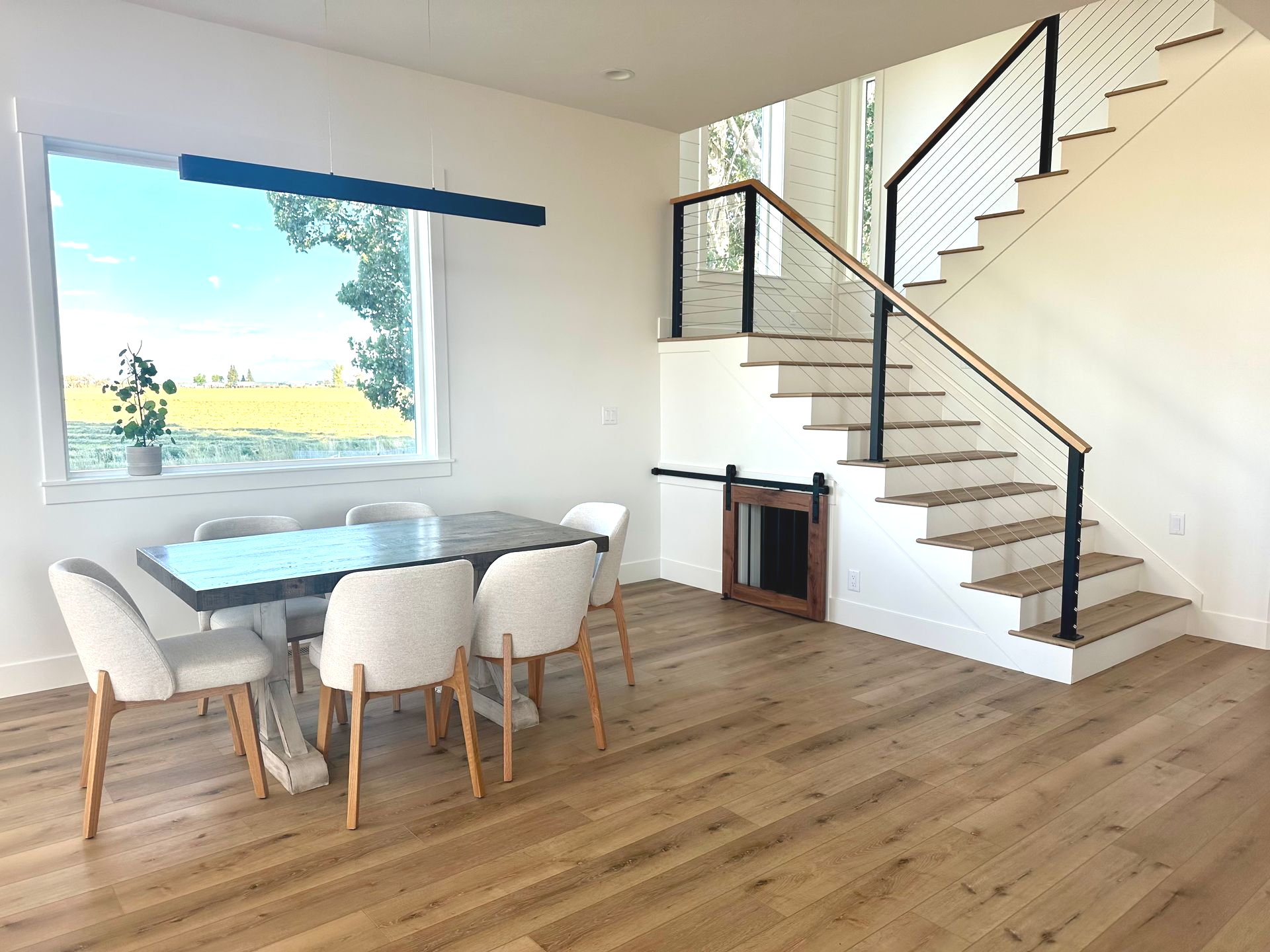 Dining room with table, chairs, stairs, window, hardwood floors, and dog door under stairs.