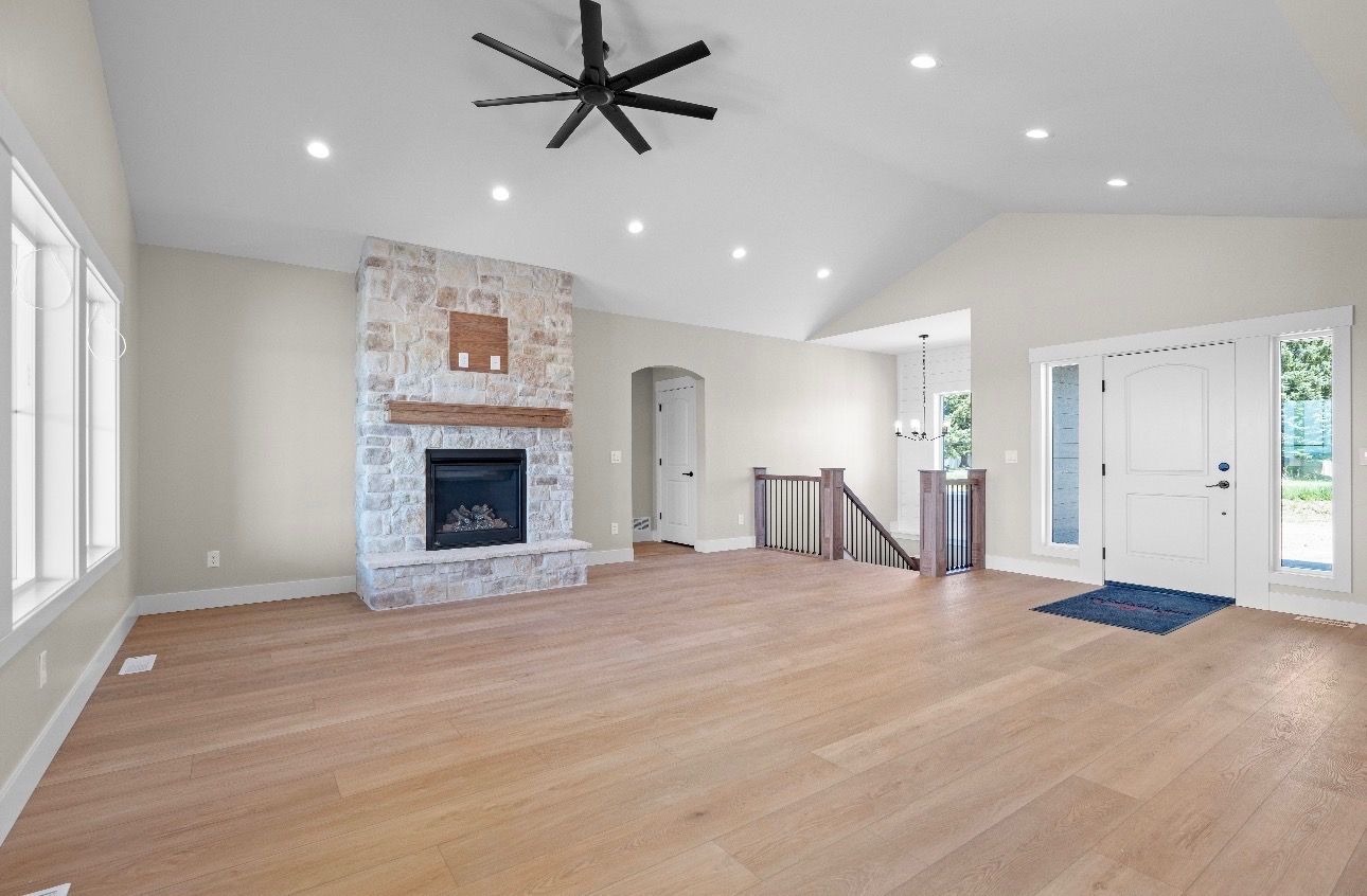 Spacious empty living room with hardwood floors, stone fireplace, ceiling fan, and large windows