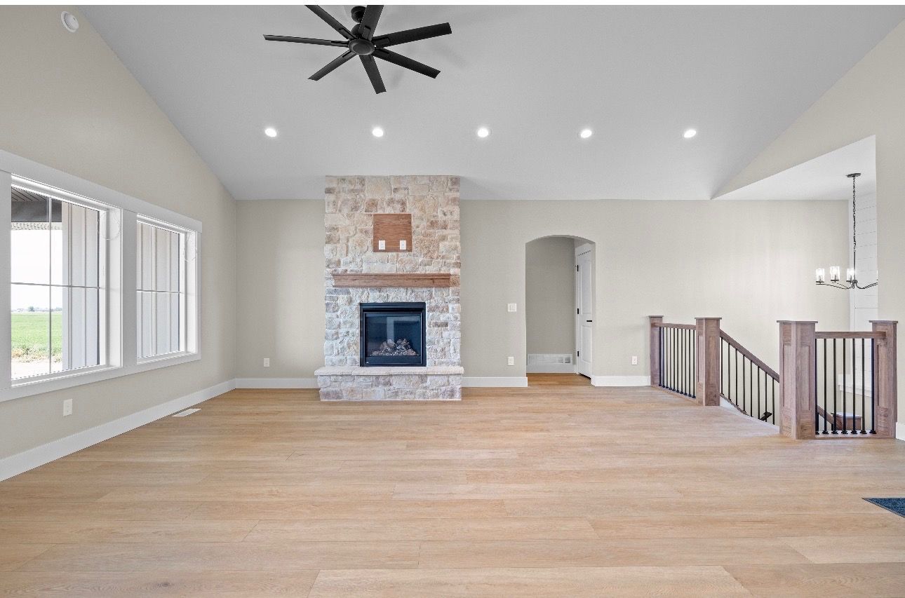 Spacious living room with wood floors, white walls, stone fireplace, recessed lights, and large windows