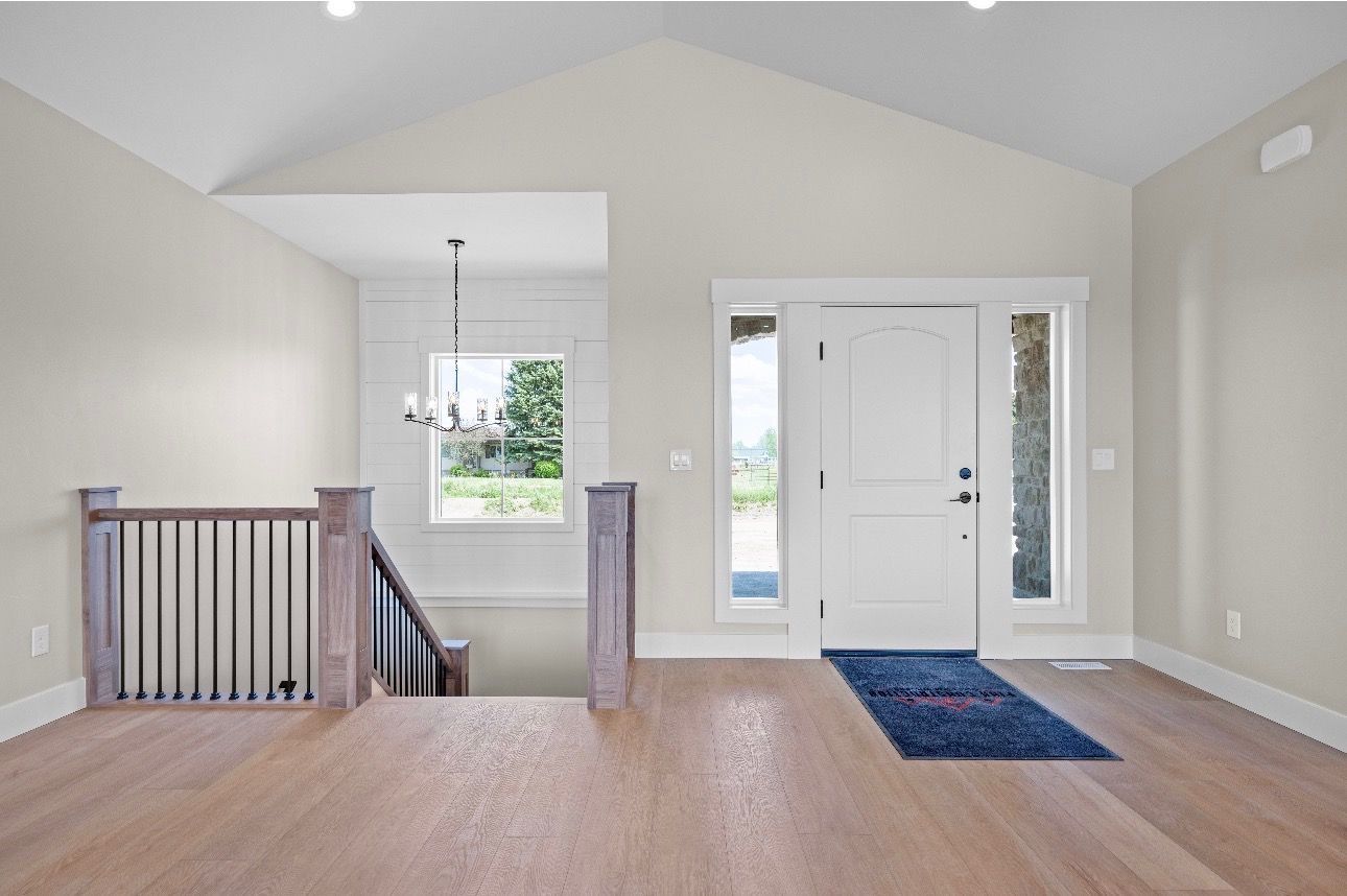 Empty modern living room with white walls, wood floor, stair railing, and front door with sidelights