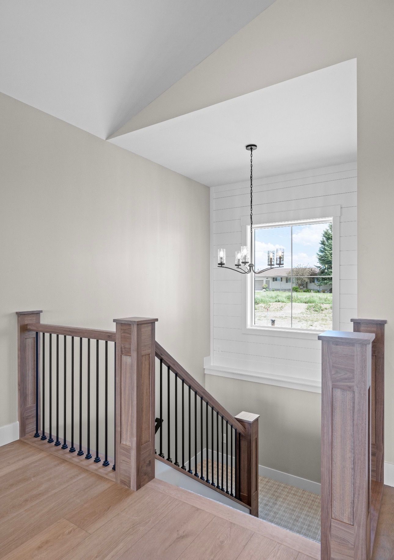 Staircase landing with wood railing, beige walls, and a window overlooking a grassy yard.