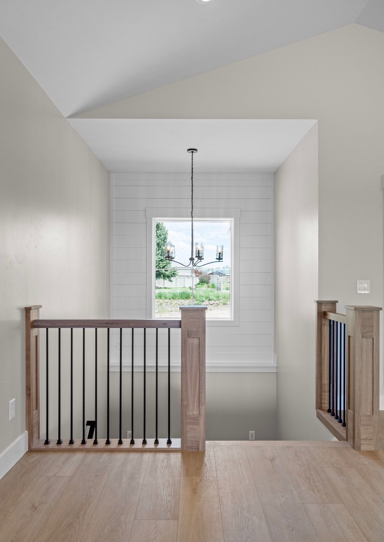 Bright hallway landing with wood floor, railing, and a window overlooking greenery