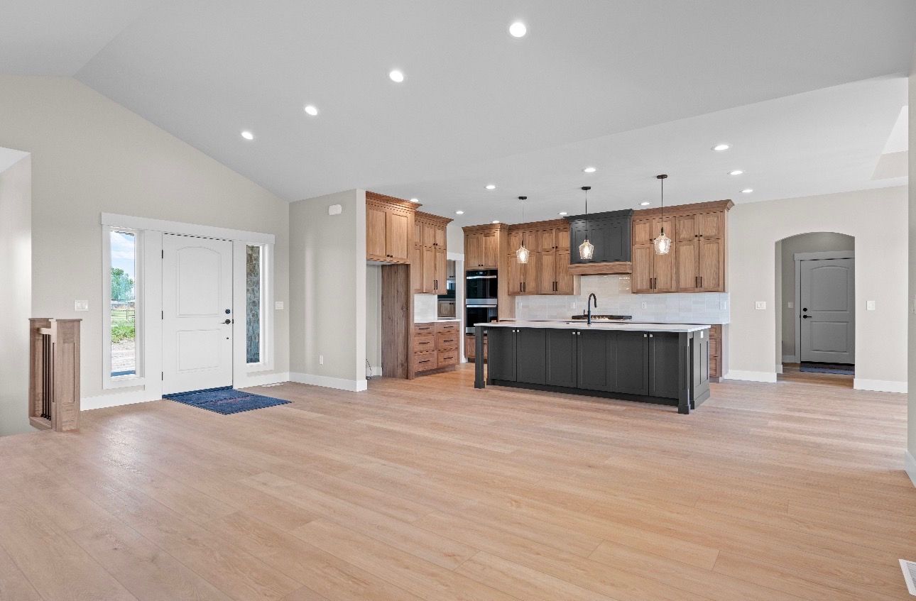 Spacious open-plan kitchen and living area with light wood floors, white walls, and modern wood cabinets.