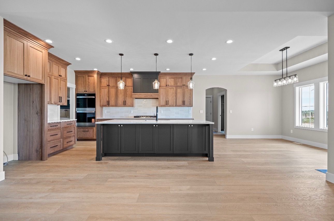 Modern open kitchen with dark island, wood cabinets, and light hardwood floors in a bright empty room