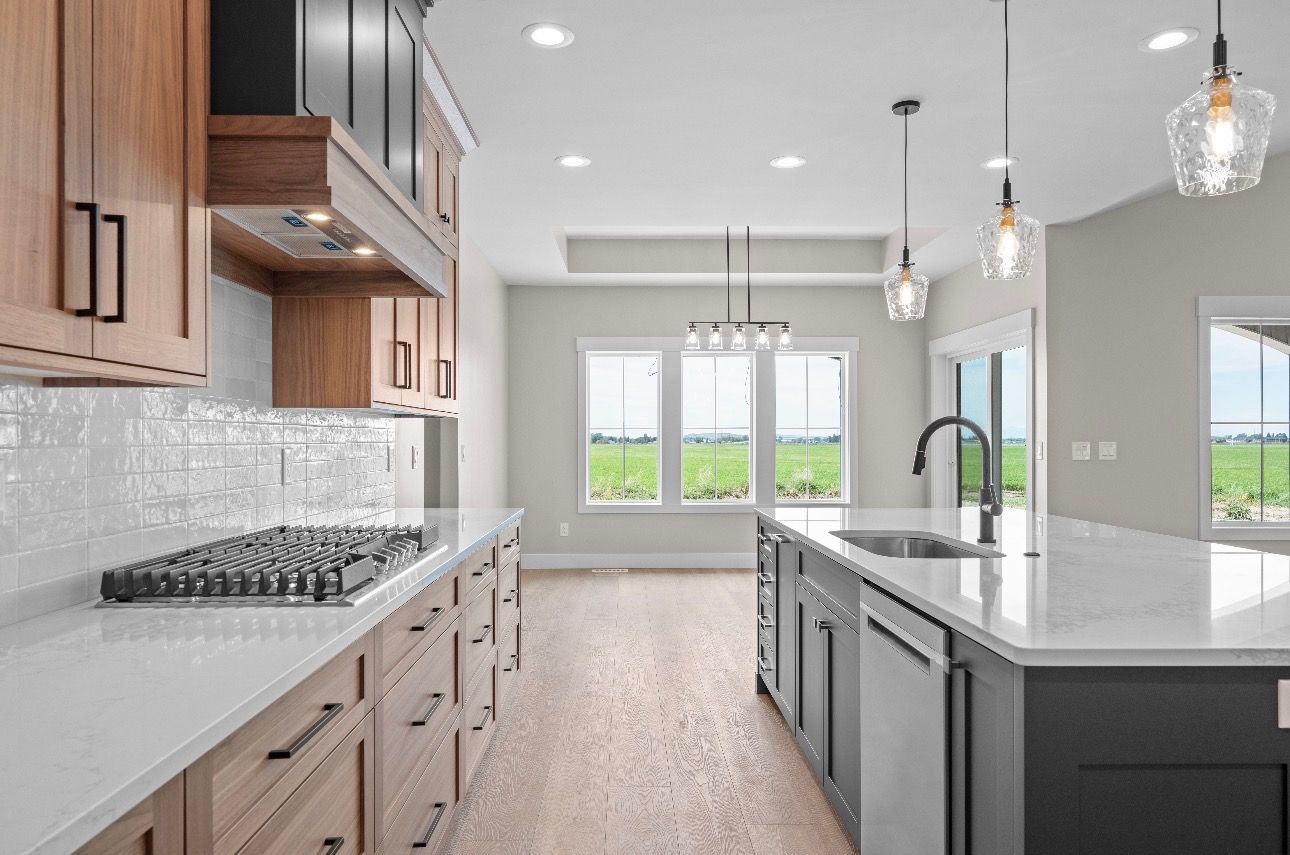 Modern kitchen with white countertops, wood cabinets, island sink, pendant lights, and bright windows