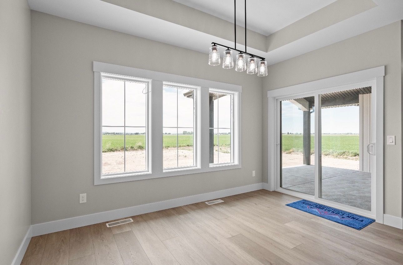 Empty modern room with light wood floors, gray walls, windows, sliding glass door, and chandelier.