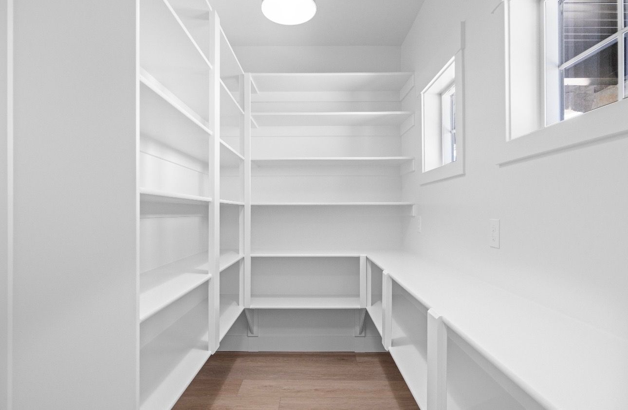 White walk-in closet with built-in shelves, hanging rods, and wood floor, lit by a ceiling light