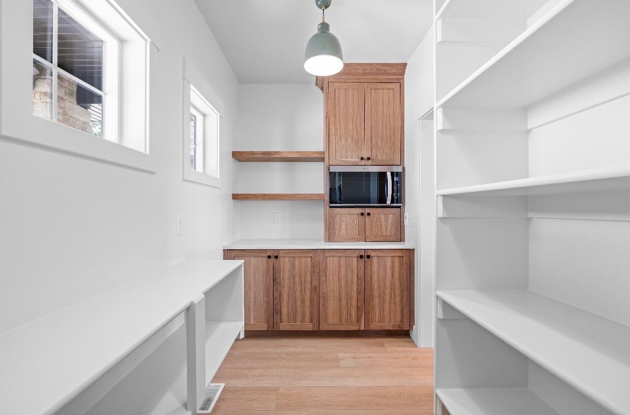Bright white walk-in pantry with wooden cabinets, shelves, and a built-in microwave at the far end.