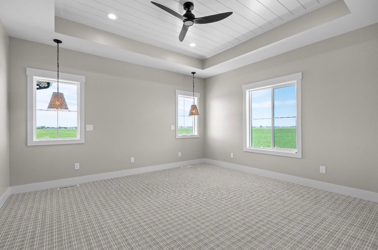 Empty carpeted bedroom with gray walls, three windows, and a ceiling fan with lights