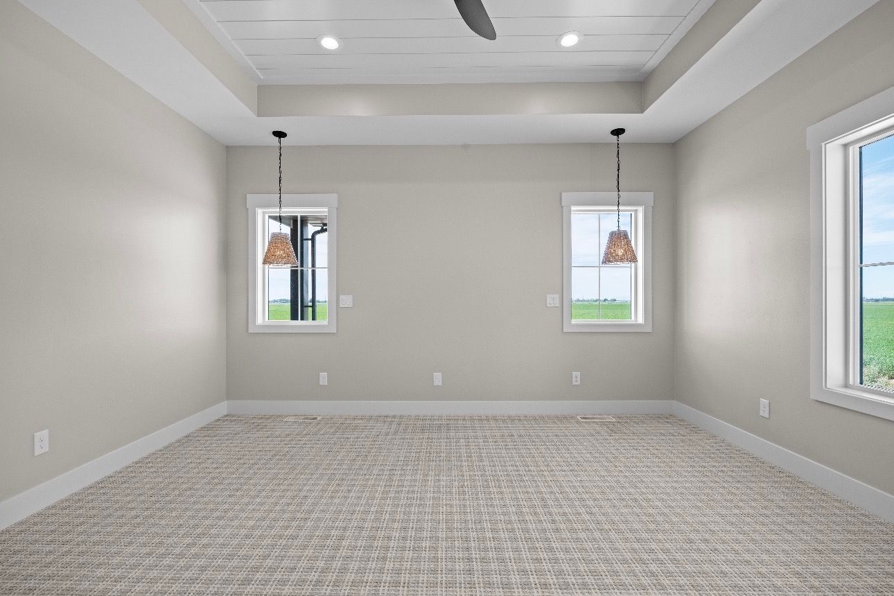 Empty beige carpeted room with gray walls, two small windows, and recessed ceiling lights.