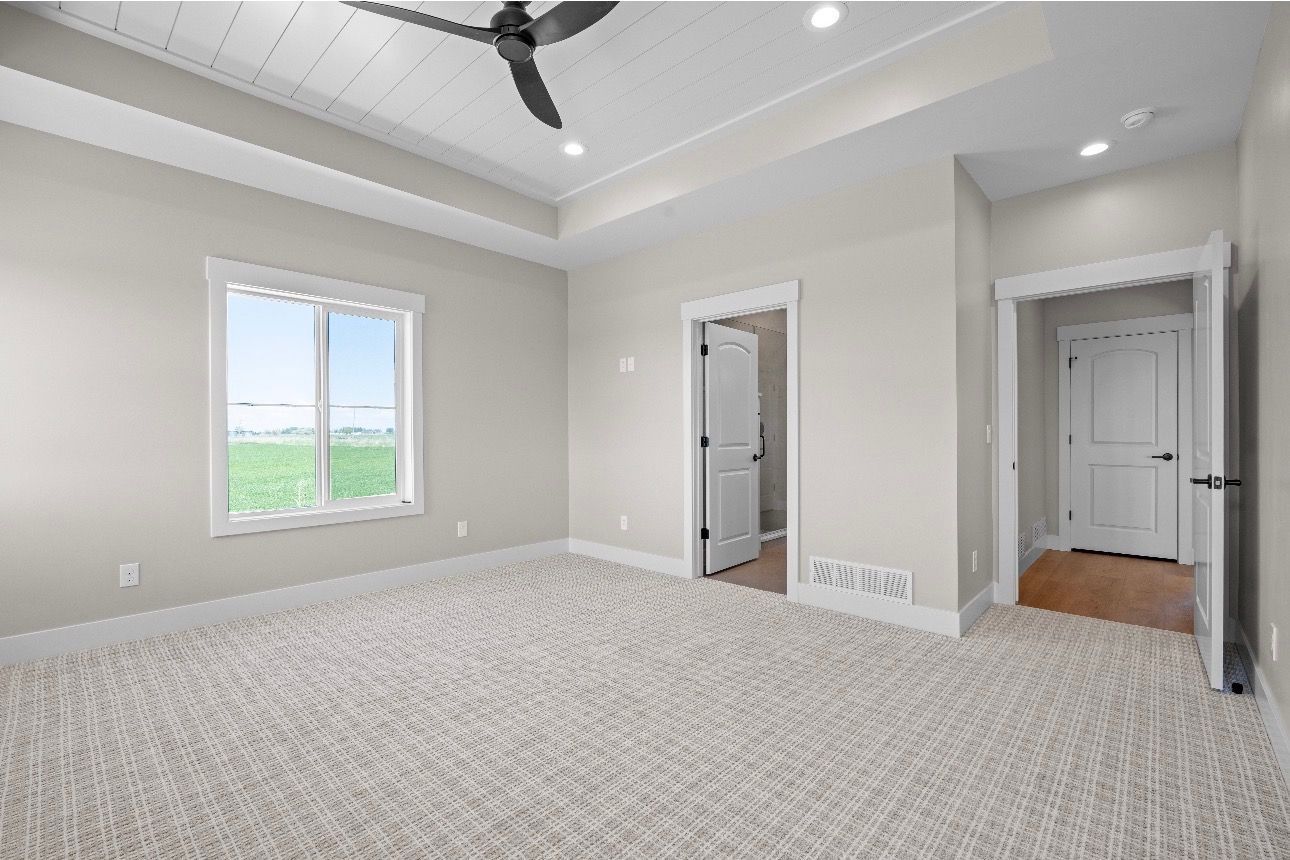 Bright empty bedroom with carpet, ceiling fan, window, and two doorways.