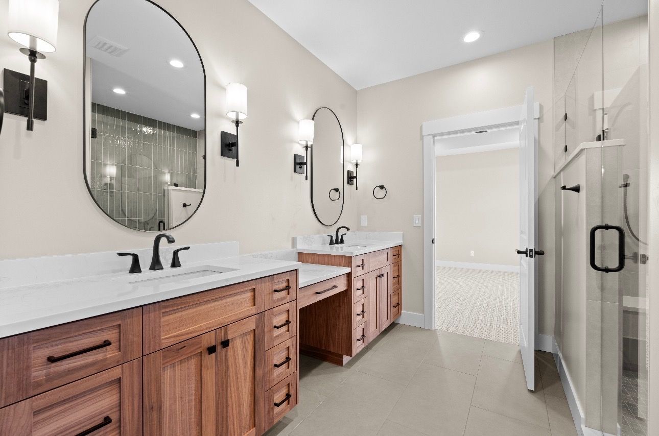Bright modern bathroom with double sinks, wood vanities, oval mirrors, and a glass shower