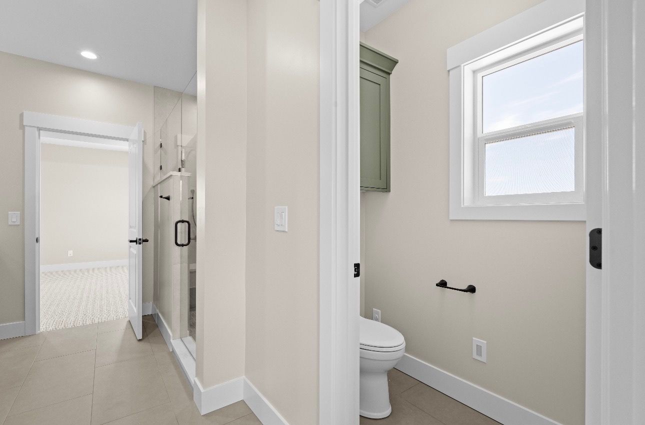 Hallway view into a small bathroom with white walls, window, toilet, and shower.