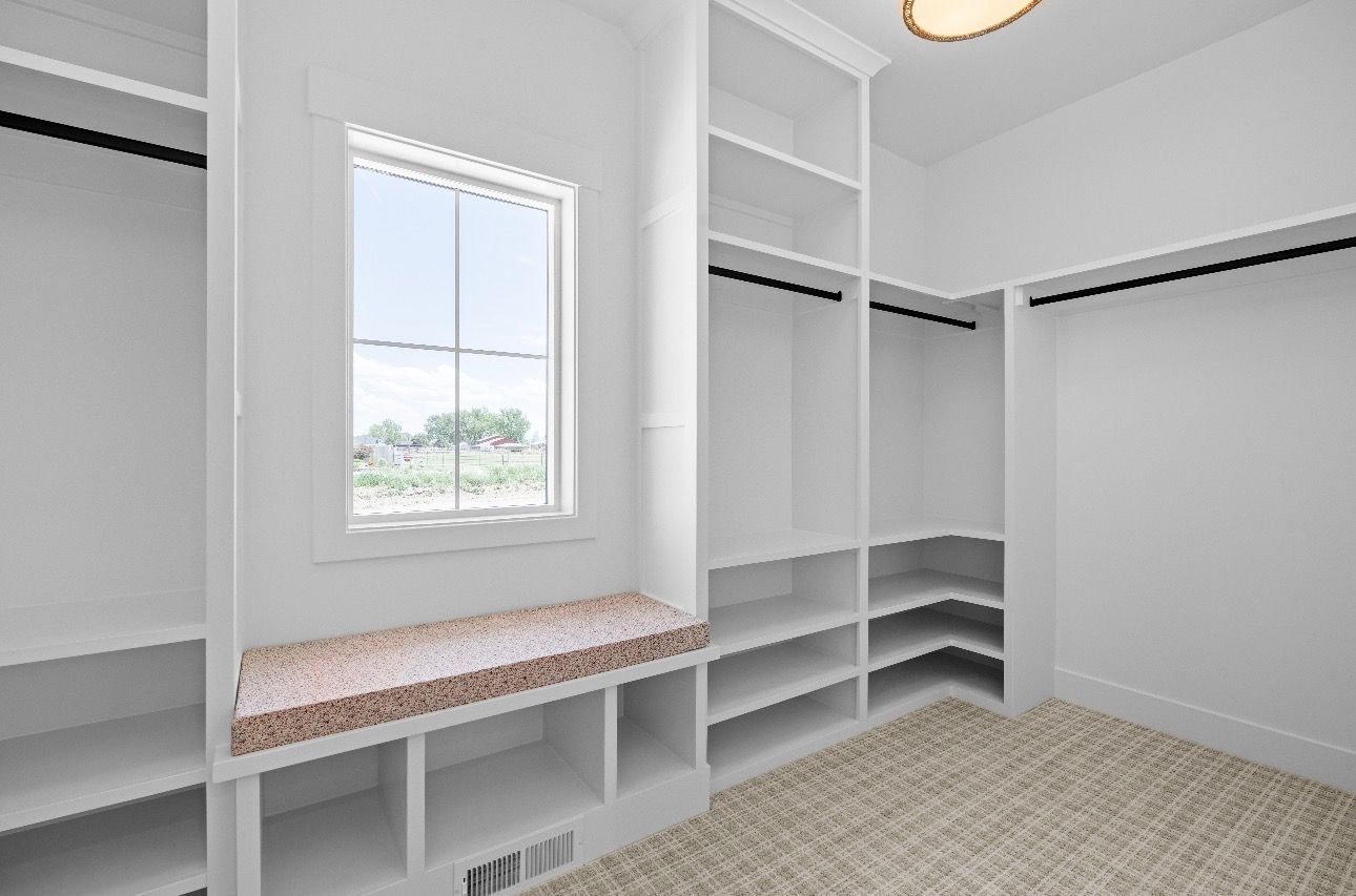 Empty white walk-in closet with built-in shelves, hanging rods, and a window over a bench.