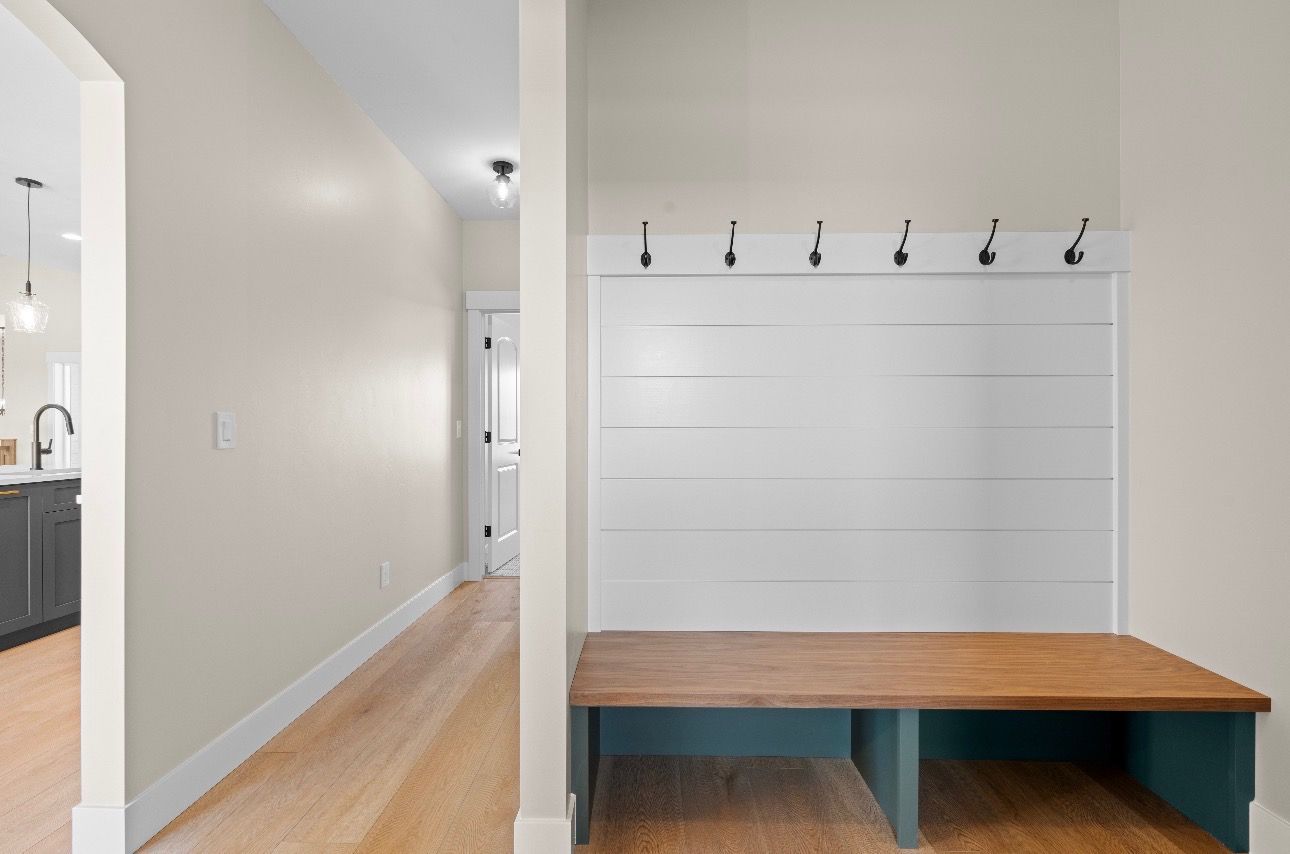Hallway with white walls, wood floor, and a wooden bench beneath wall hooks and a mirror panel