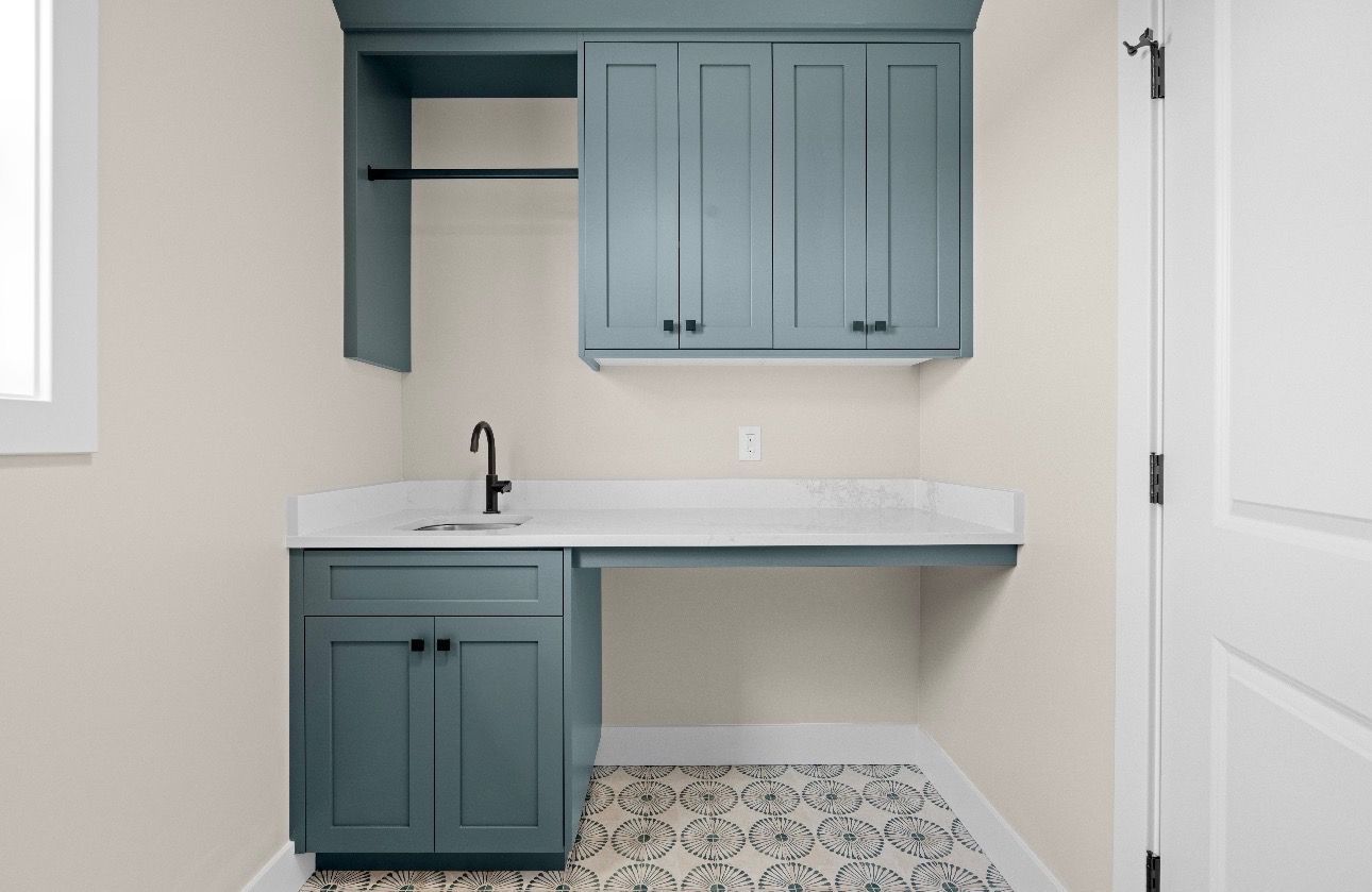 Small teal kitchenette with sink, cabinets, marble countertop, and patterned tile floor.