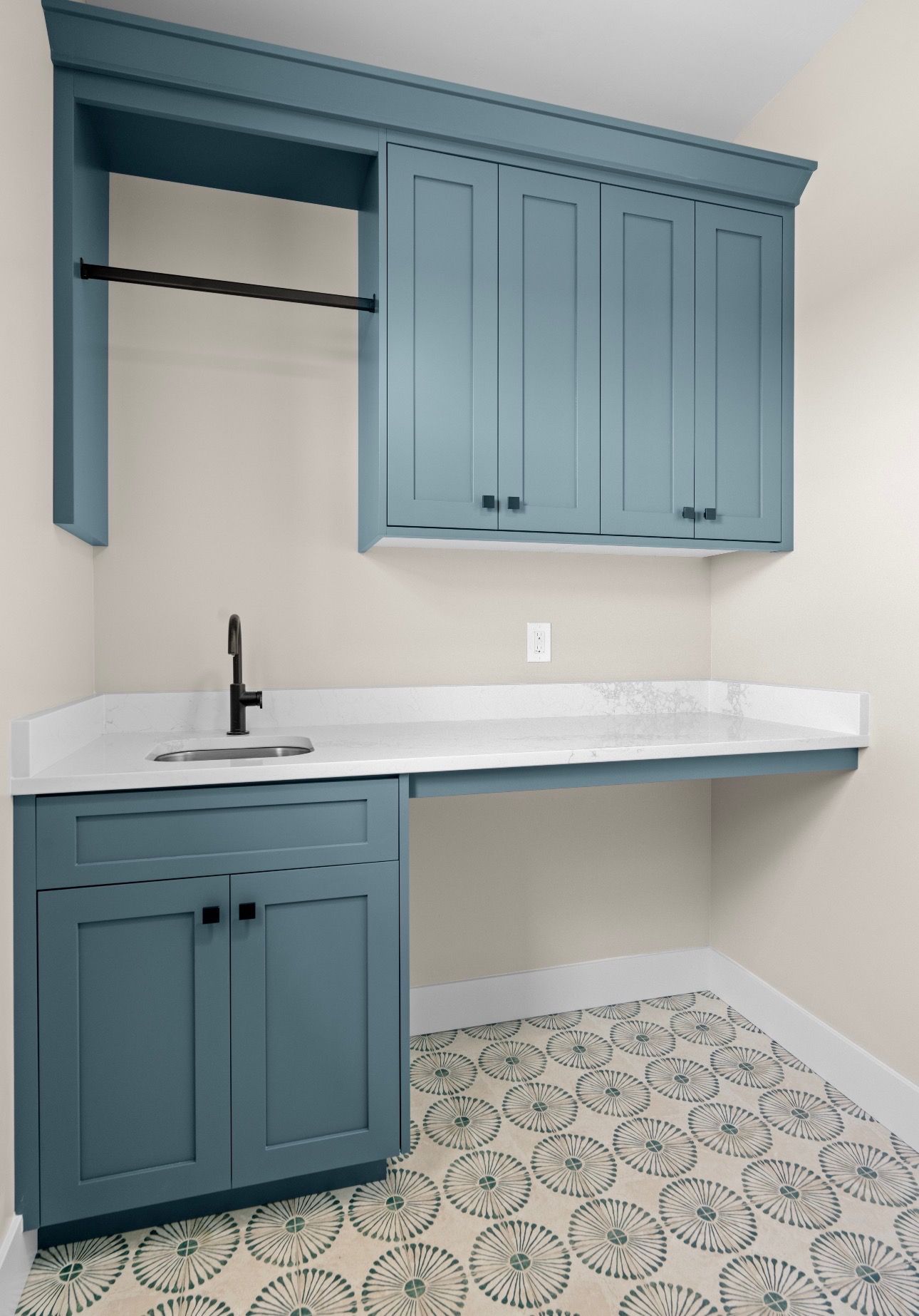 Blue laundry room with sink, counter, and upper cabinets on patterned tile floor