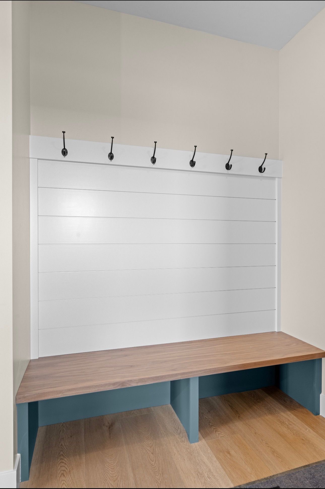 Built-in bench with wood top, blue base, and white slatwall hooks in a small retail display nook