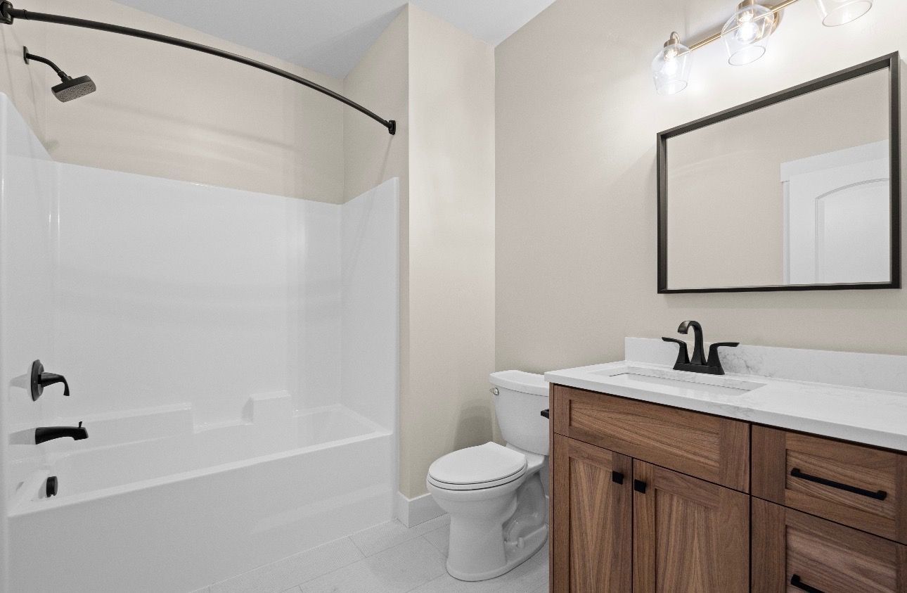Bright bathroom with white tub, black fixtures, and wooden vanity with mirror
