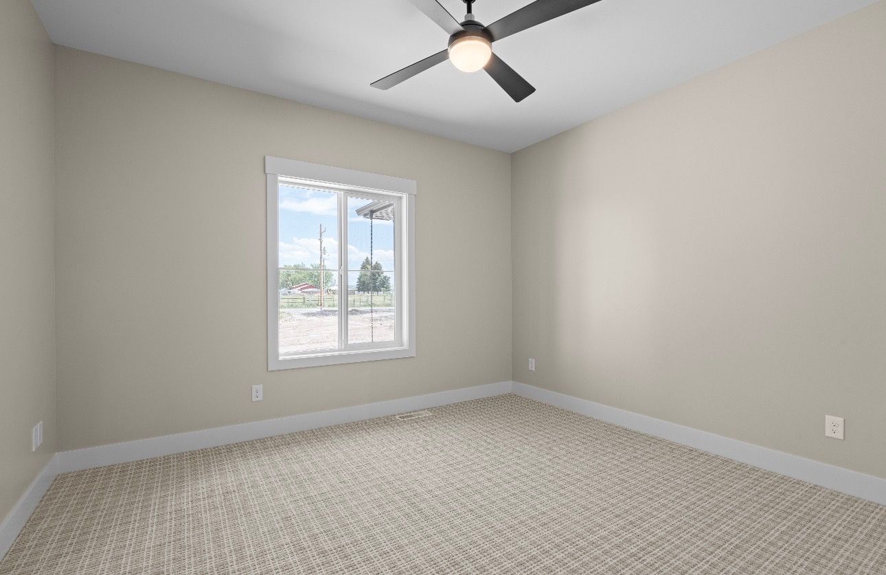 Empty beige bedroom with carpet, ceiling fan, and a window letting in daylight.