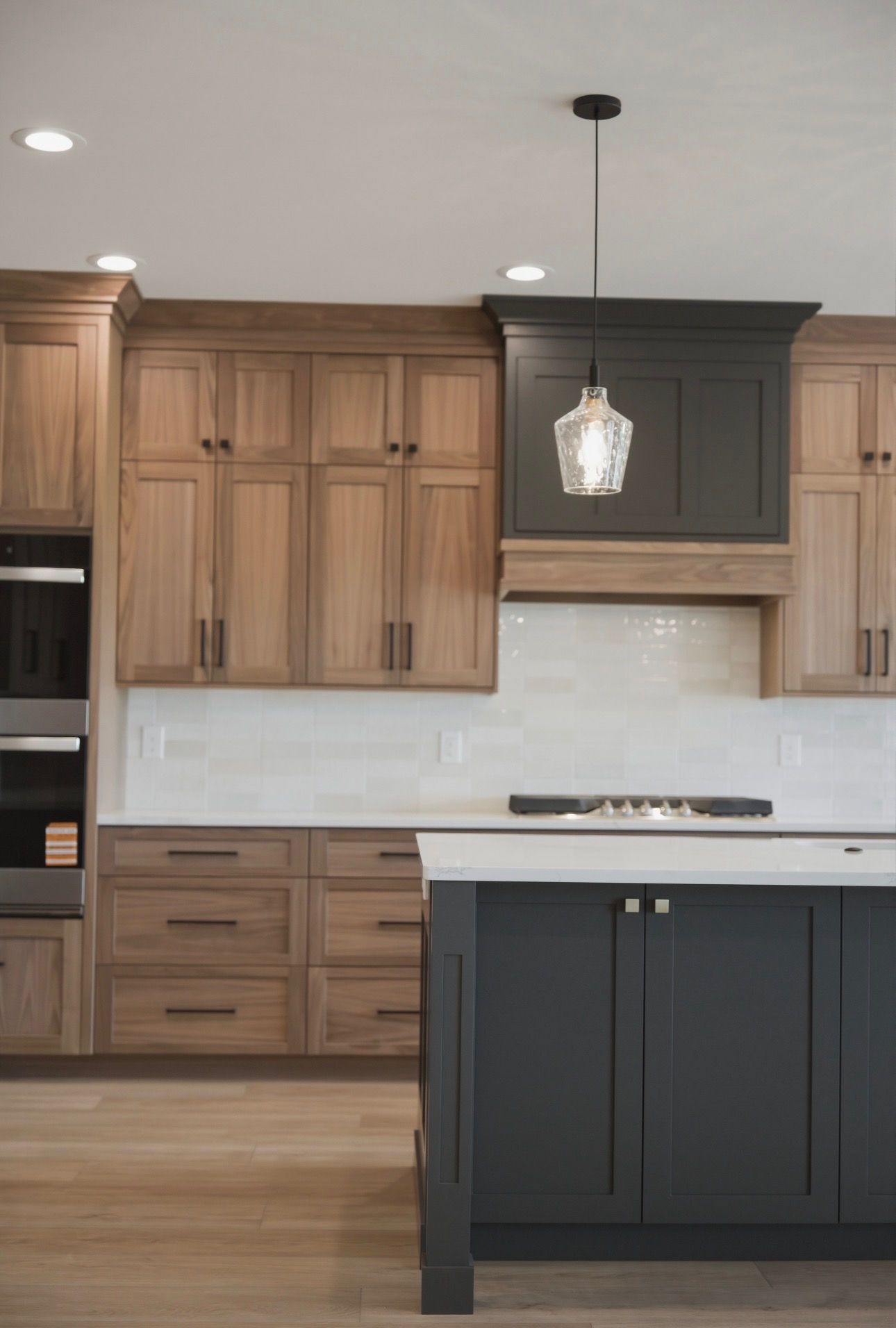 Modern kitchen with wood cabinets, dark island, white backsplash, and pendant light