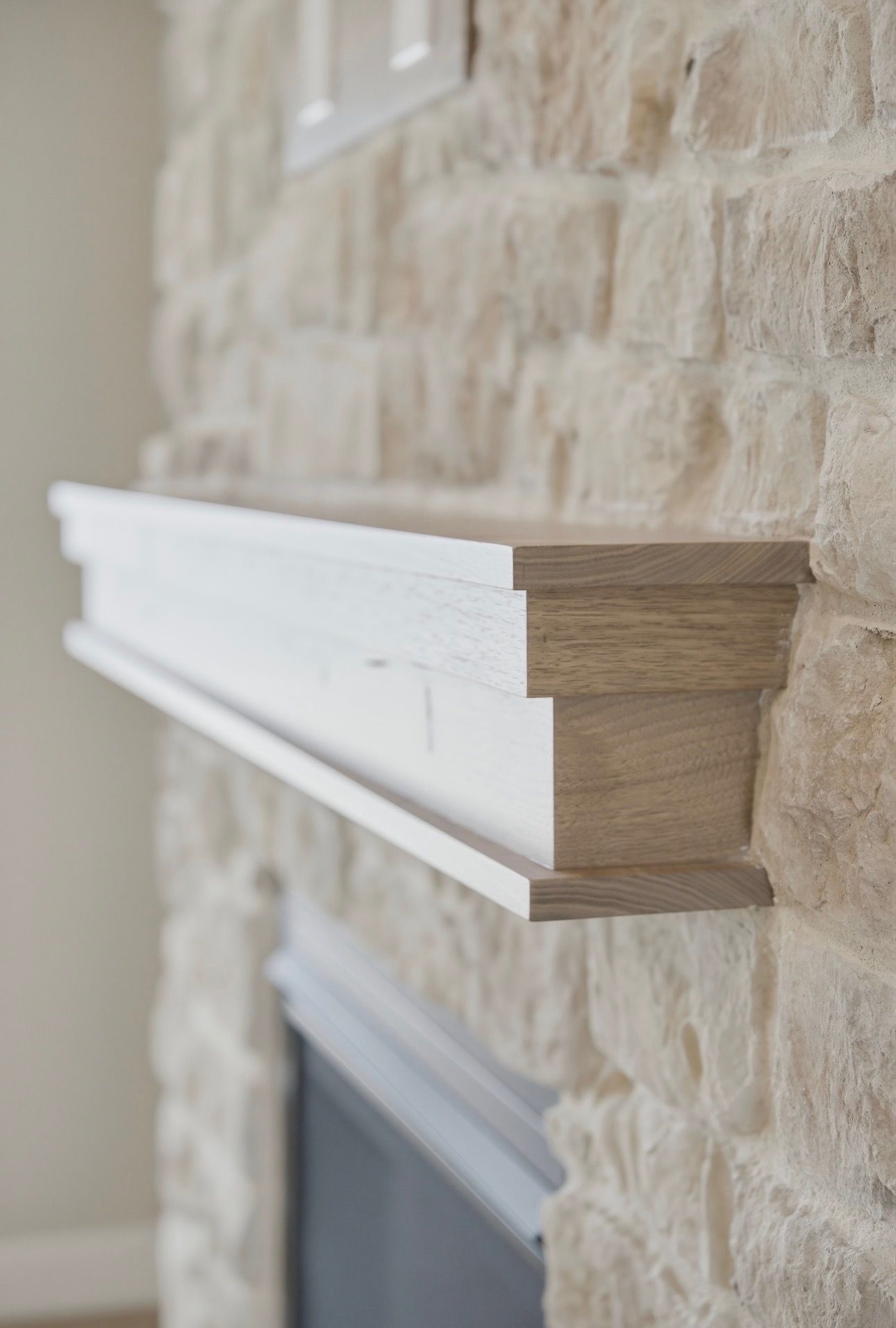 White mantel shelf on a beige stone fireplace wall