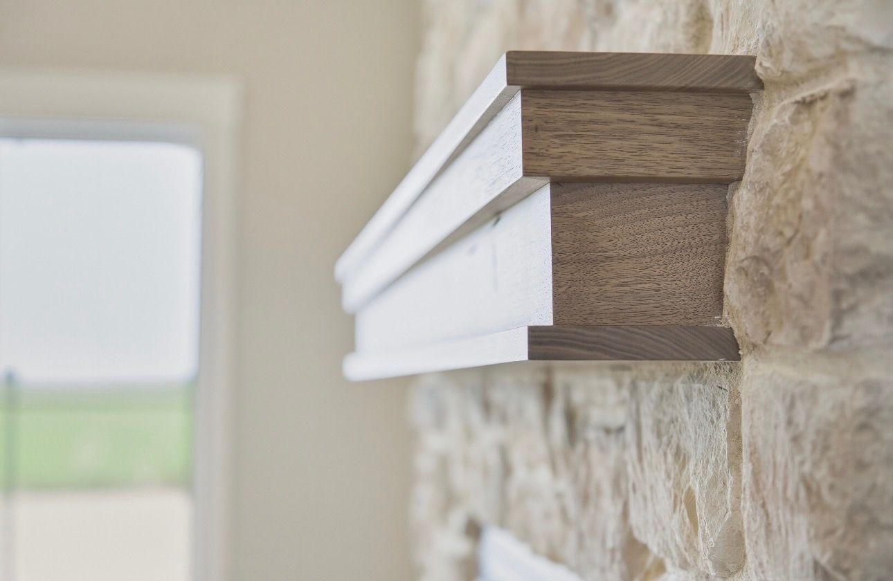 White mantel shelf mounted on a stone fireplace wall in a bright room