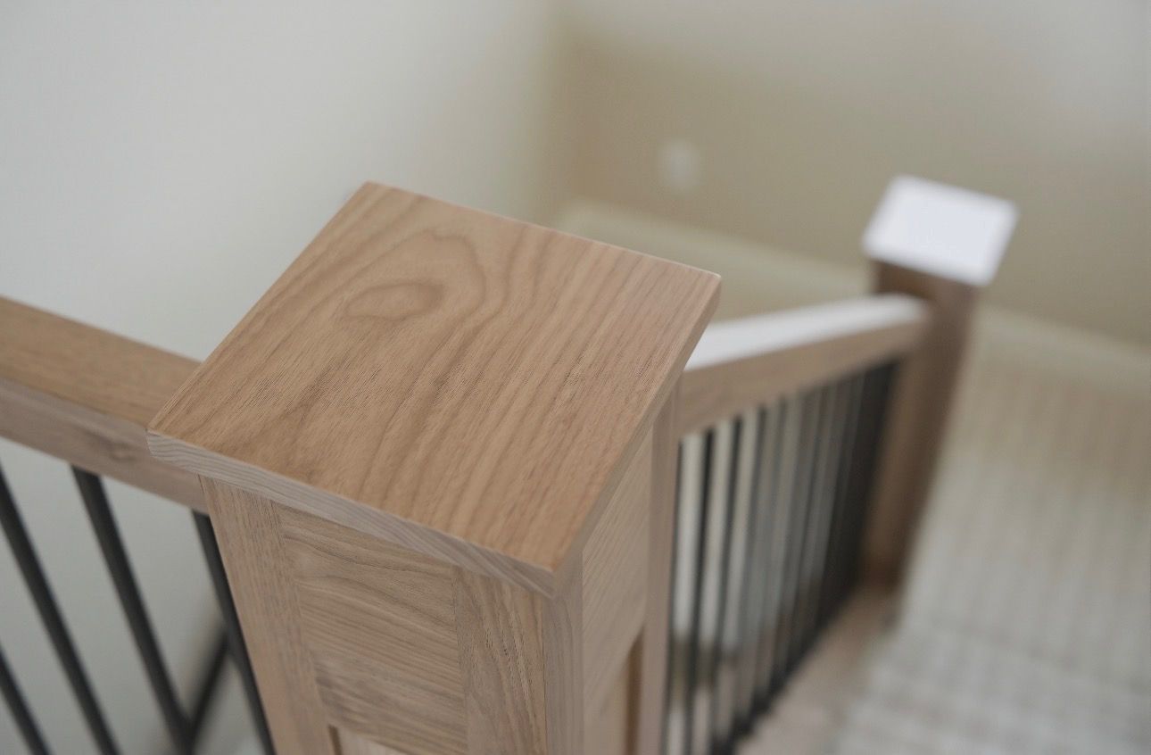 Wooden stair railing with square post and black balusters by a carpeted staircase