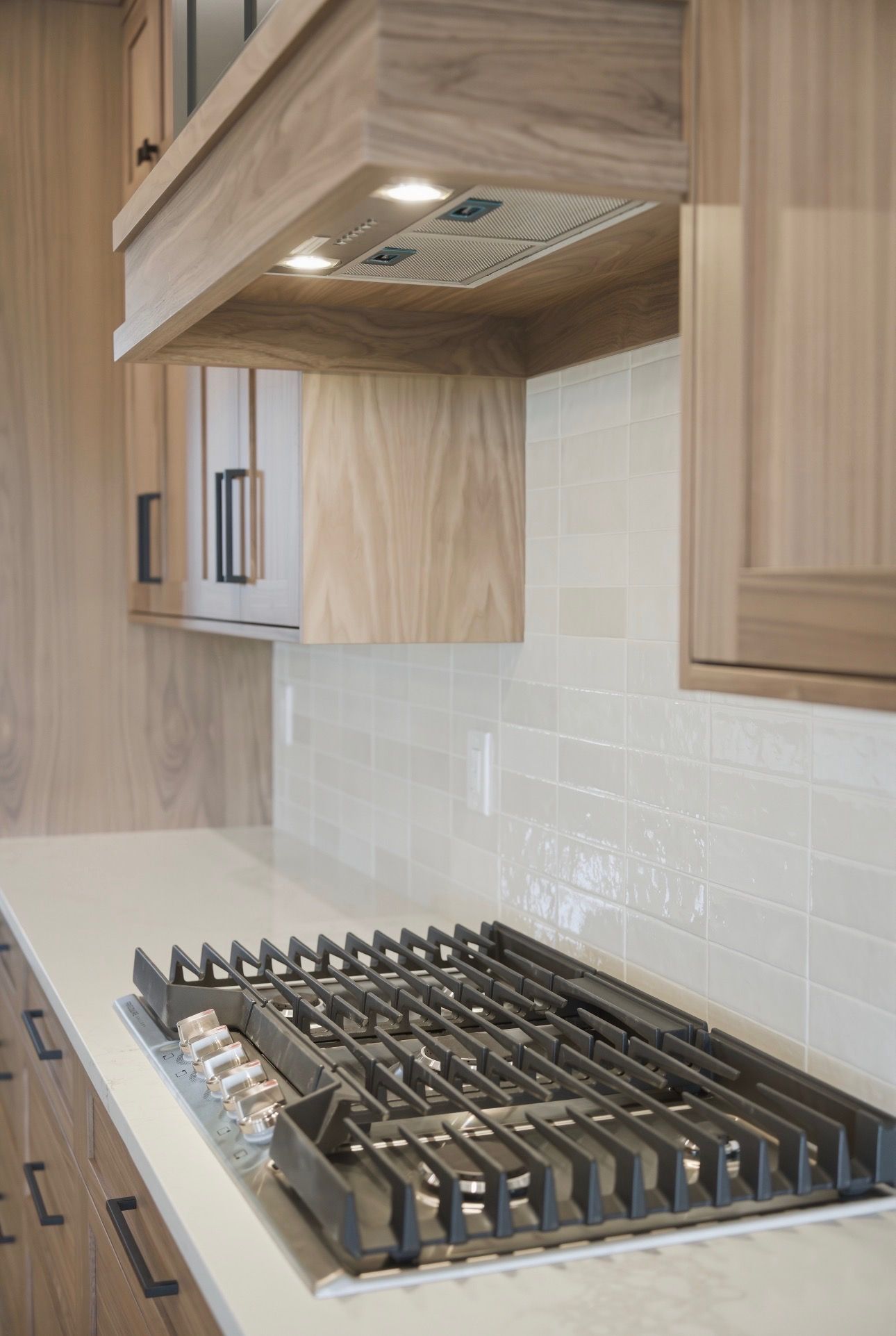Modern kitchen with wood cabinetry, white tile backsplash, and stainless steel gas cooktop under a vent hood
