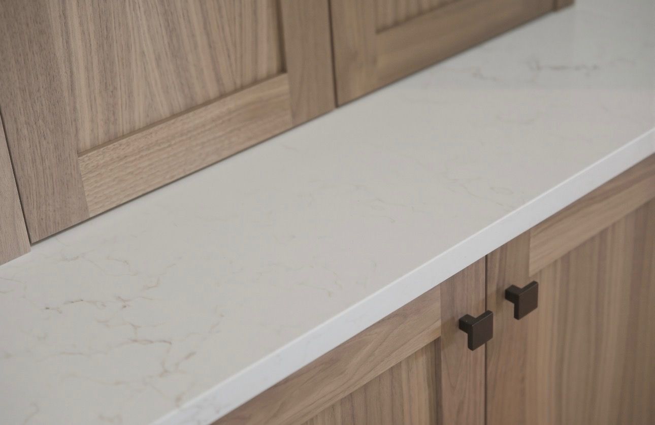 White stone countertop with light wood cabinets and black pulls in a kitchen corner