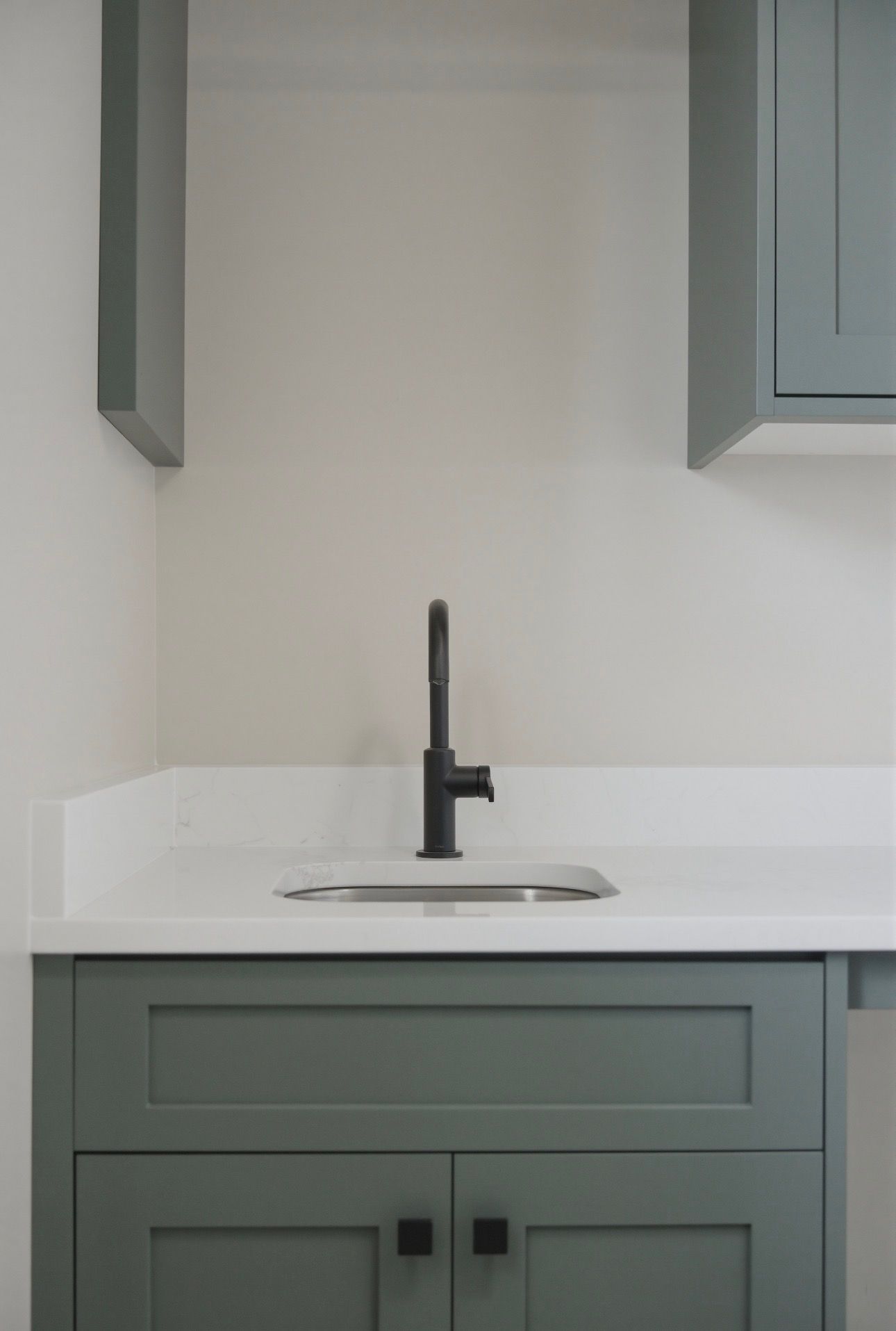 Sage green bathroom vanity with black faucet and white countertop, flanked by wall cabinets.